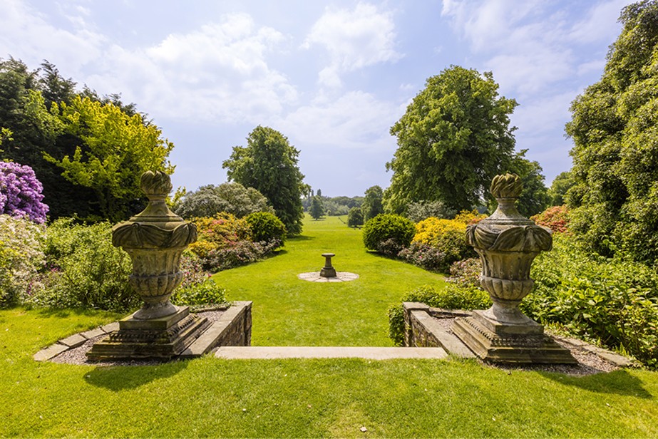 Formal English garden with stone urns and open parkland, representing orderly trust structures and long-term family planning in the United Kingdom.