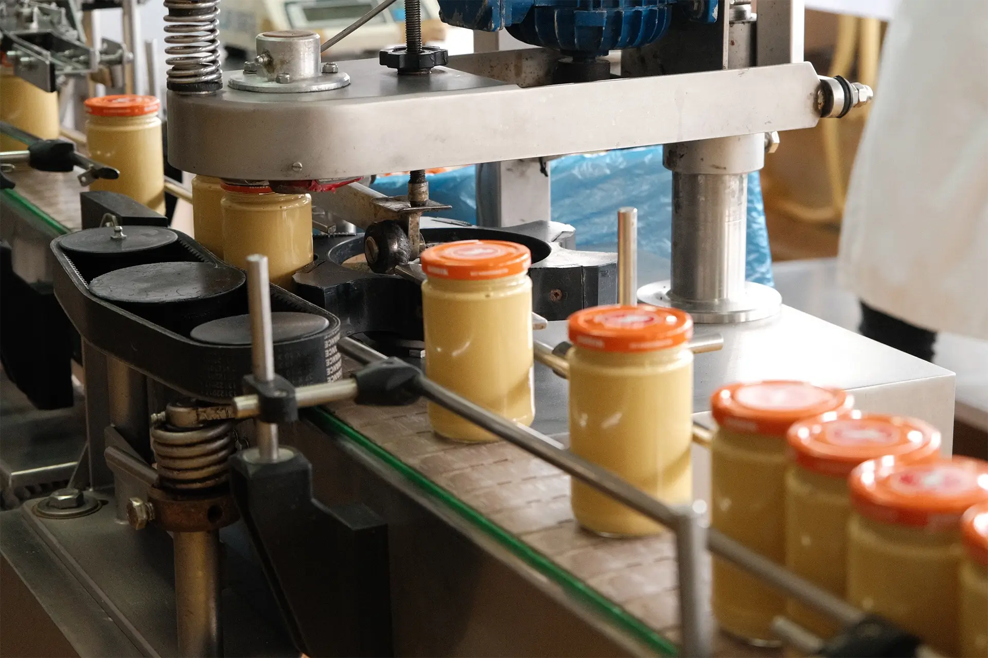 Linia produkcyjna musztardy firmy Konik: słoiki z pomarańczowymi zakrętkami przesuwają się na taśmociągu wewnątrz maszyny zamykającej.