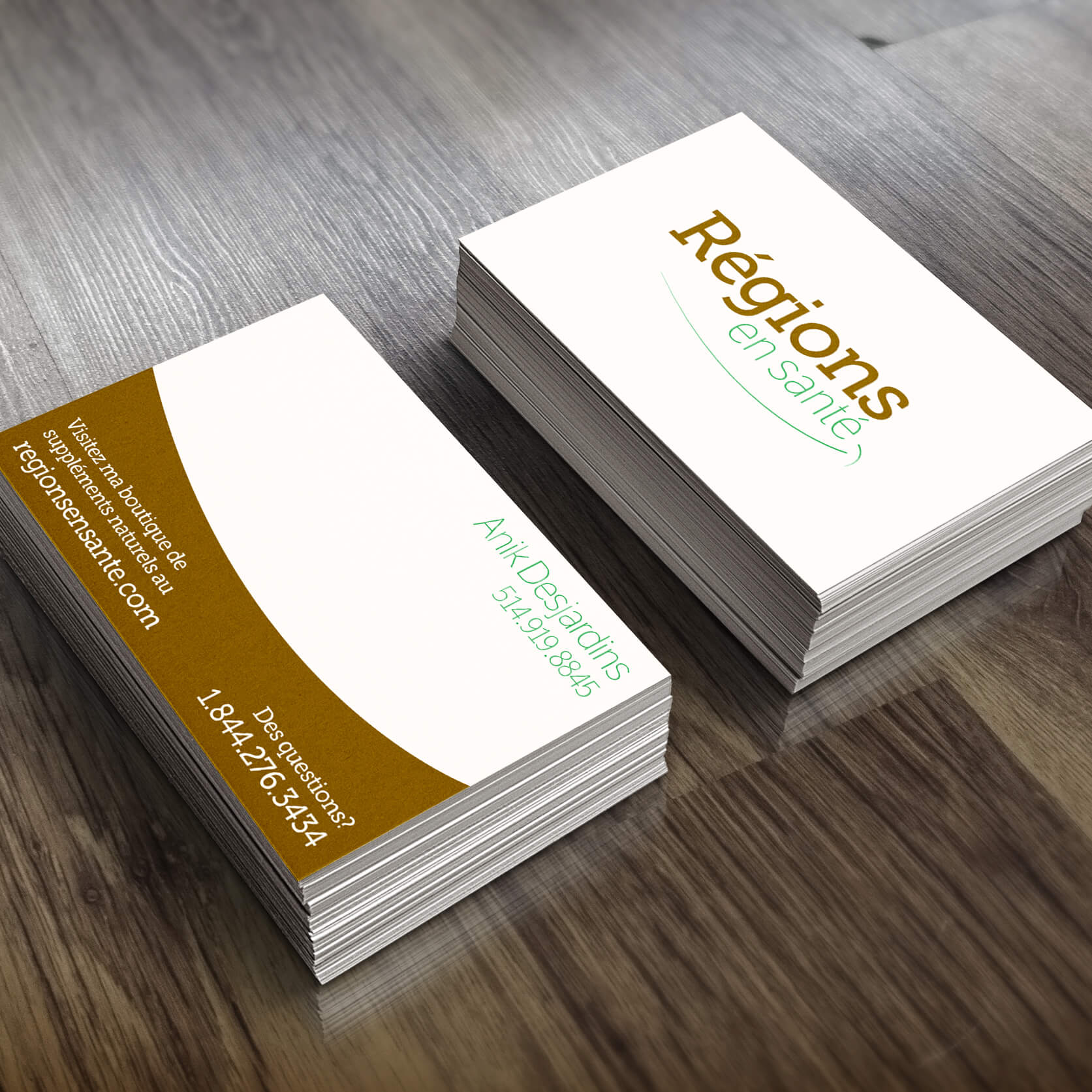 Two stacks of business cards for 'Régions en santé,' displayed on a wood surface. One stack shows the front of the card with the company’s name in brown and green modern typography. The other stack shows the back, featuring a name and a phone number in green text, along with a brown curved section containing the website URL and another phone number in white text.