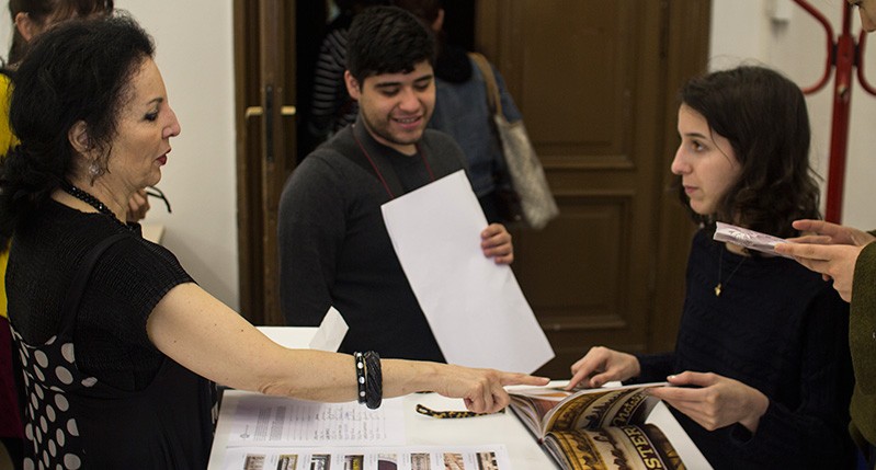 two women pointing at book and men holding paper