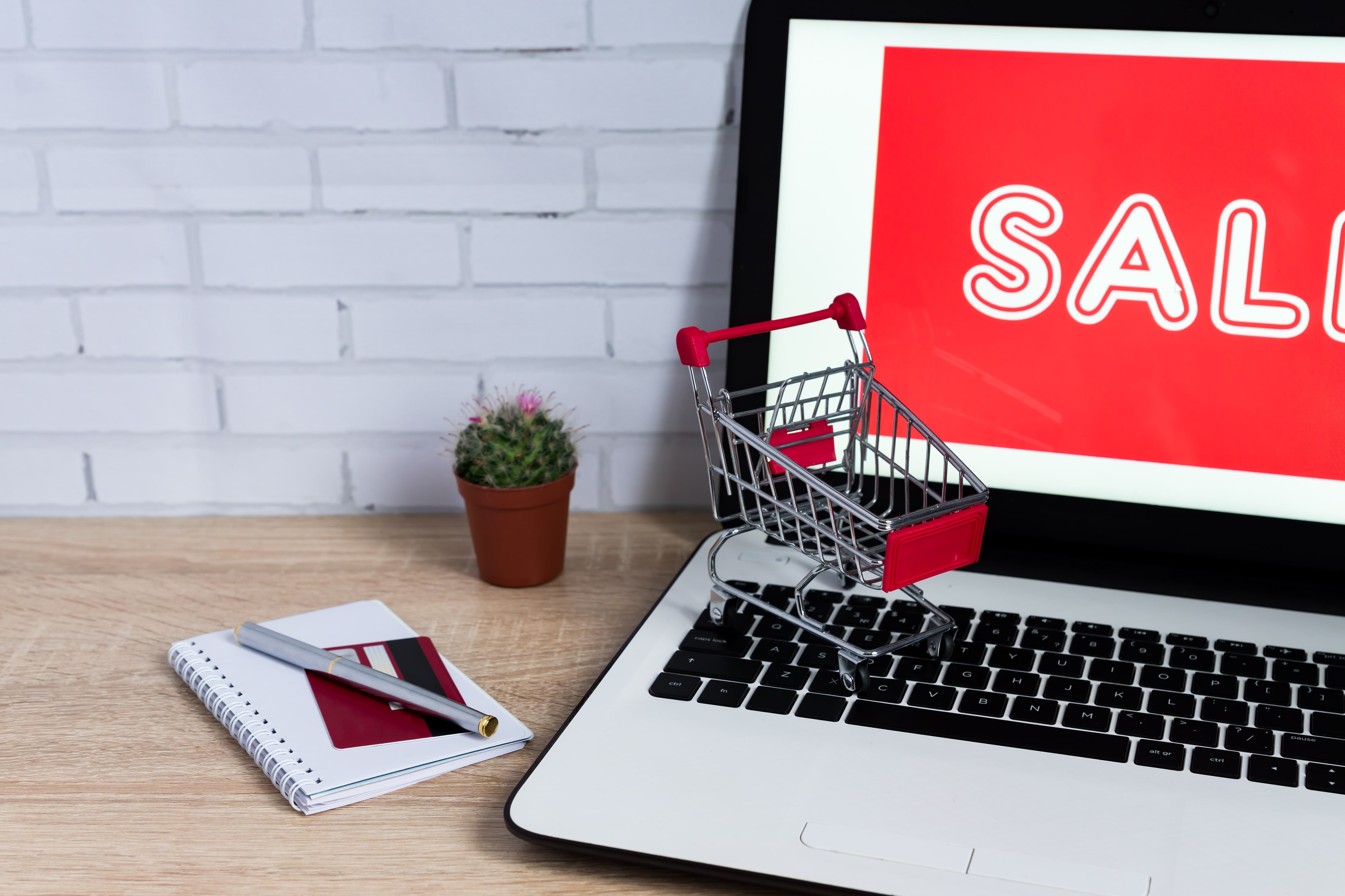 E-commerce concept for an online sale, featuring a miniature shopping cart on a laptop keyboard with a red "SALE" sign on the screen.