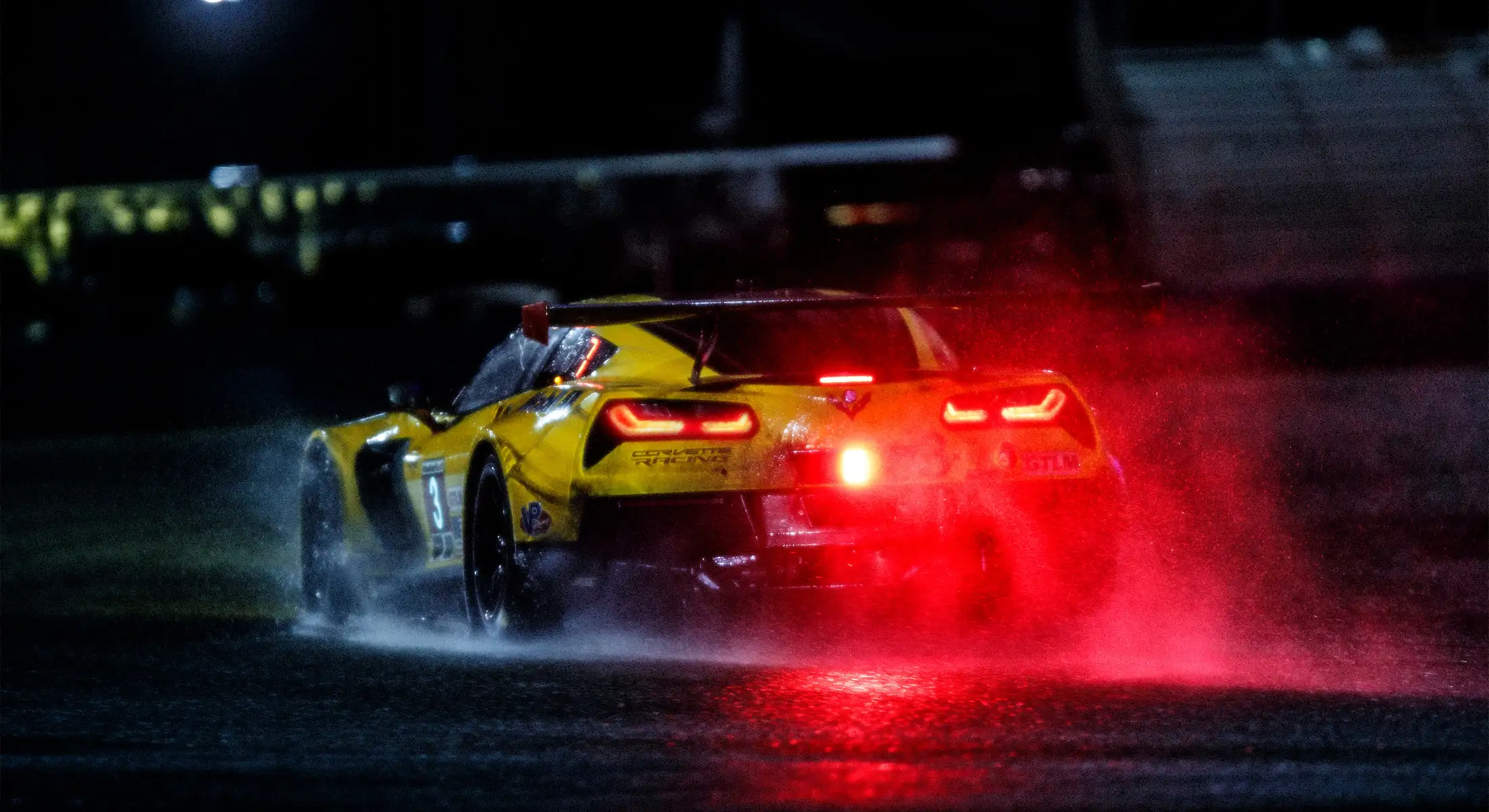 A yellow racecar driving in rain.