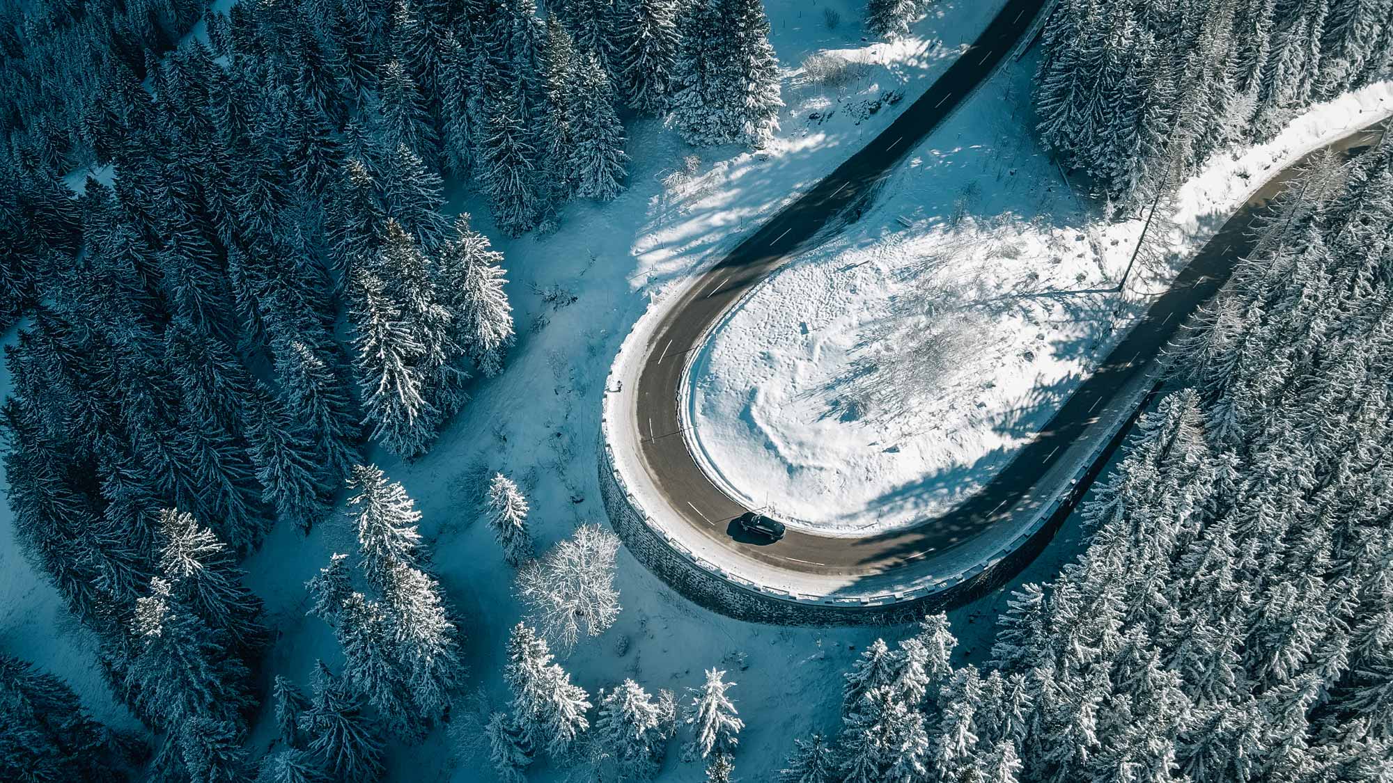FPV drone captures a car on a snow-covered curved road in a forest for Porsche Filmproduction