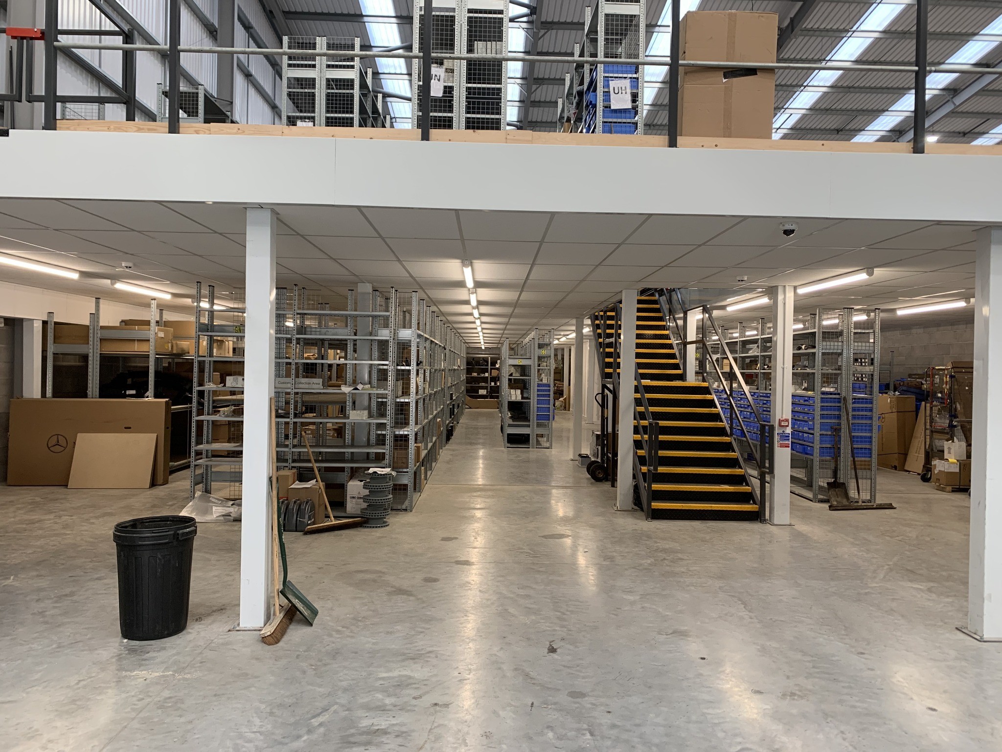 Storage shelving and a mezzanine staircase with overhead lighting.