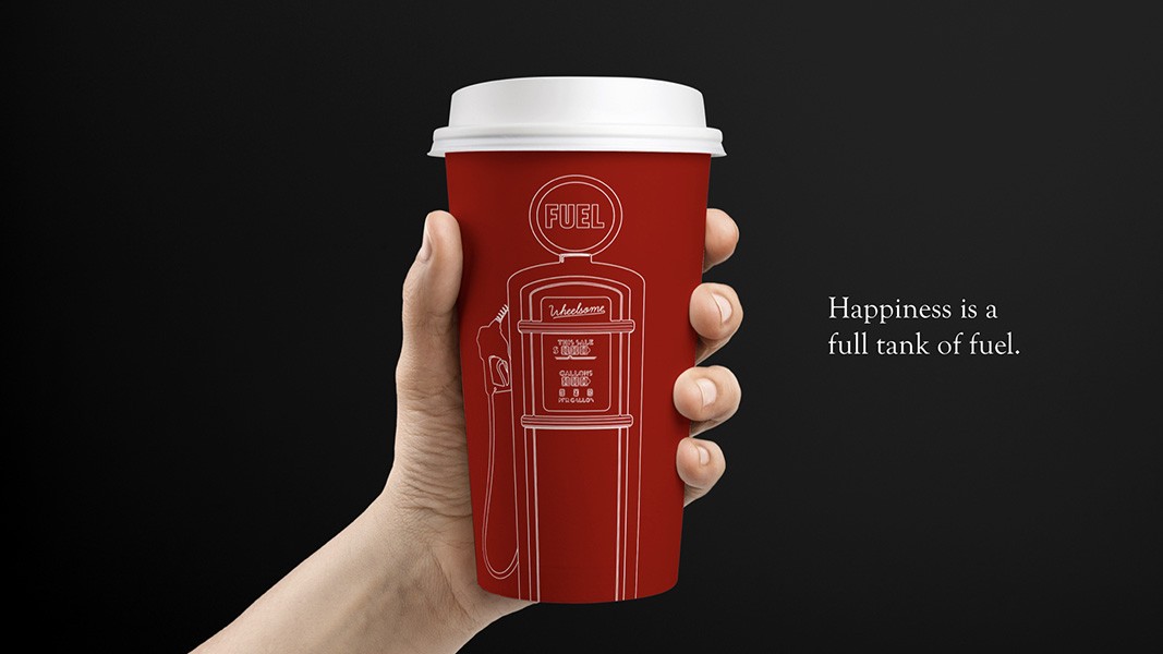 A hand holds a red disposable coffee cup with a white lid. The cup features a white line drawing of a gas pump and the word "FUEL" printed on it. The background is black, and the text "Happiness is a full tank of fuel" is displayed to the right of the cup.