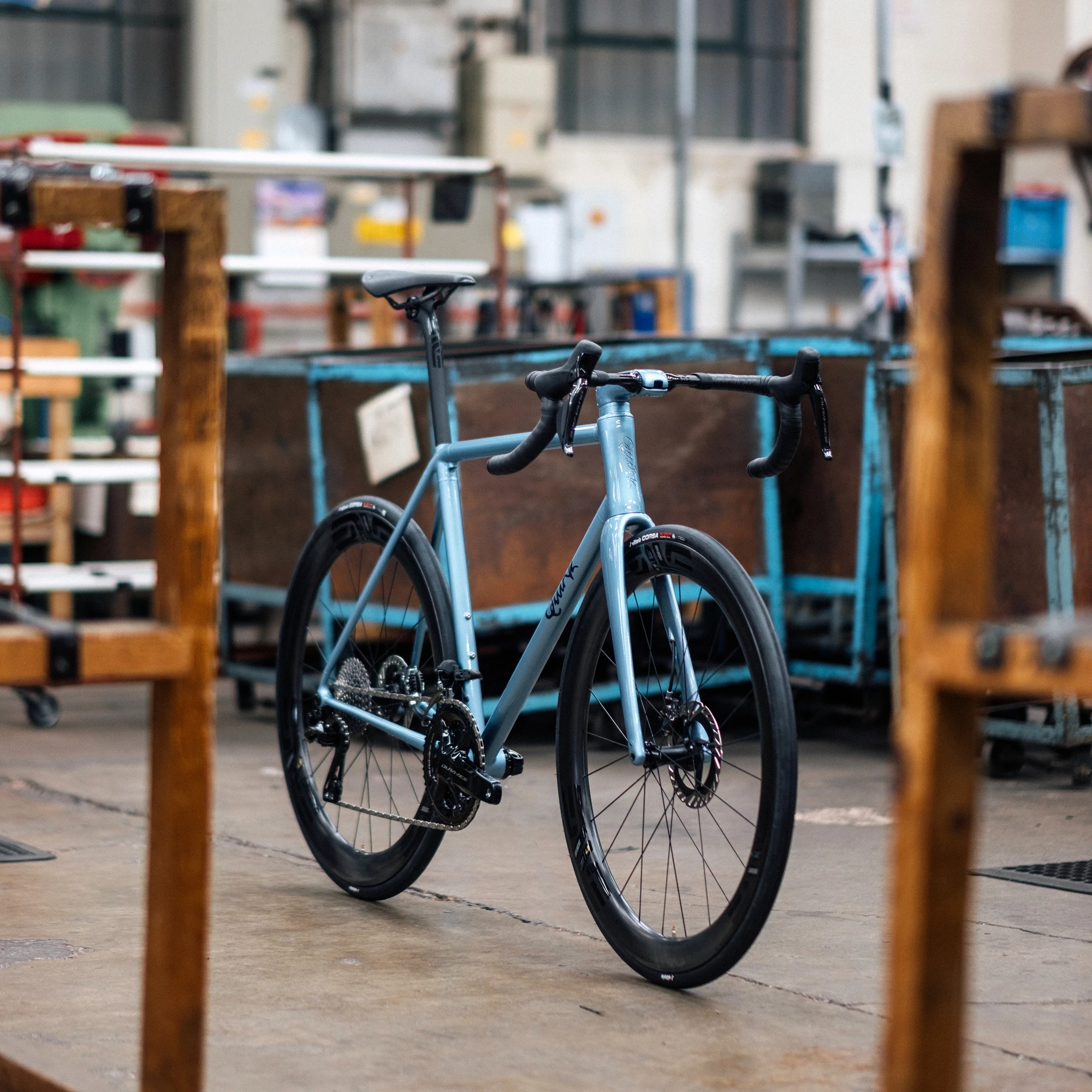 Light blue Quirk Cycles Durmitor road bike in a workshop with dark wheels