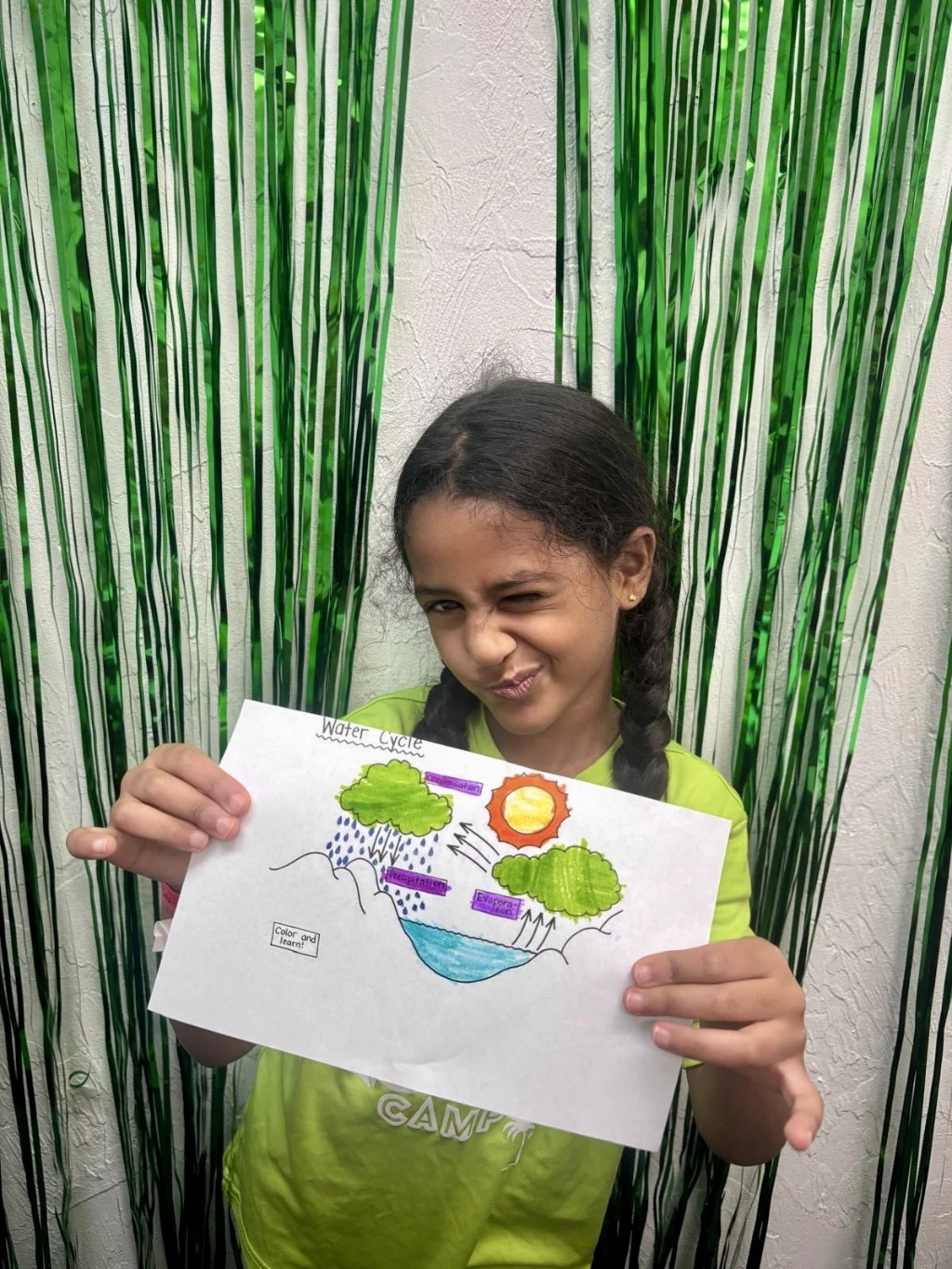 Girl holding up a science drawing winking at the camera.