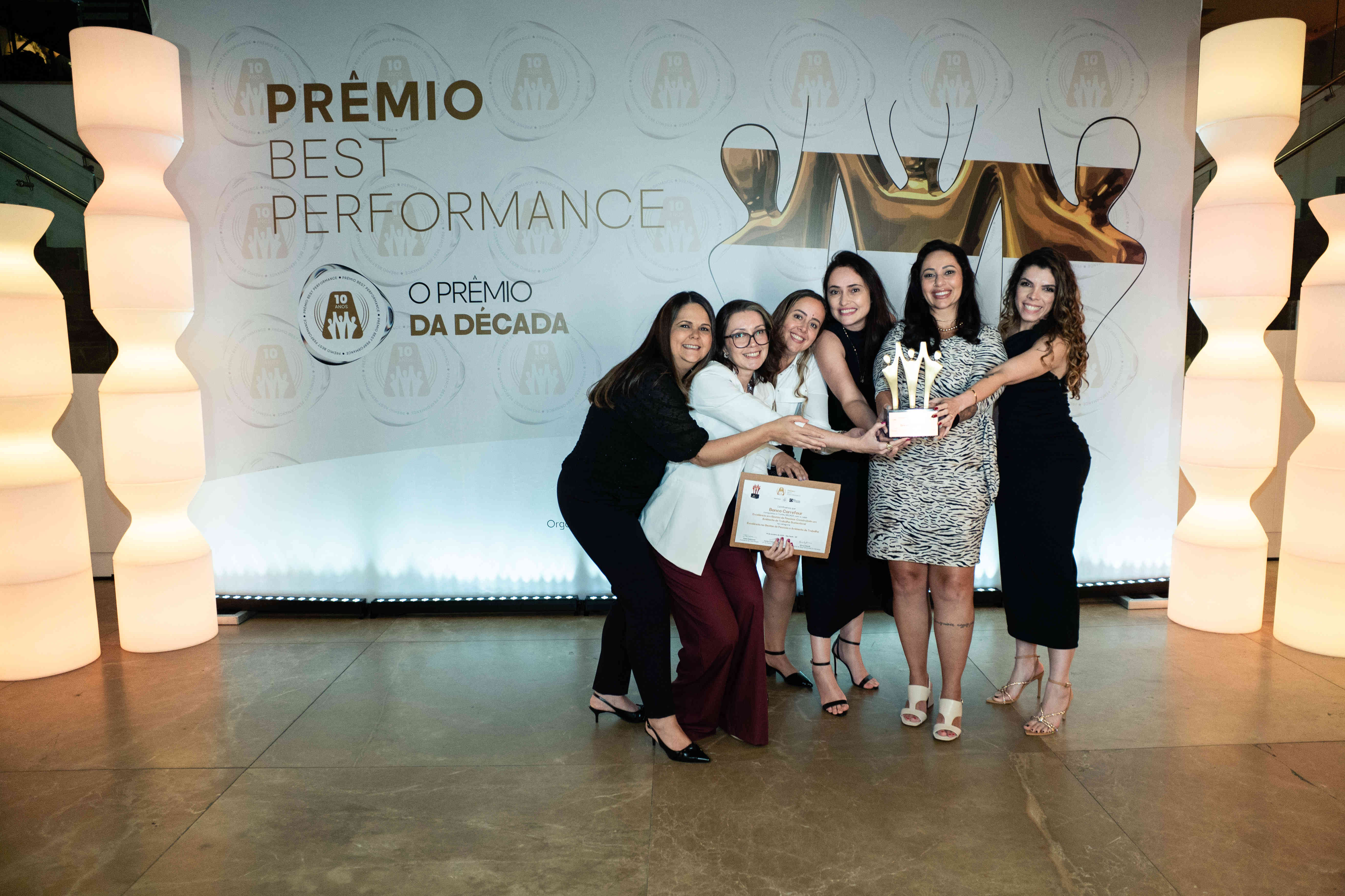 Executivos do Banco Carrefour posando com troféu bronze e certificado no palco do Prêmio Best Performance 2025.