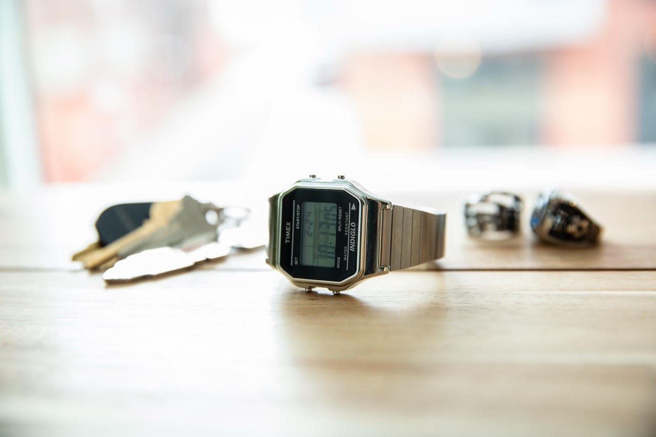 Metal digital wristwatch resting on a wooden table in soft window light.