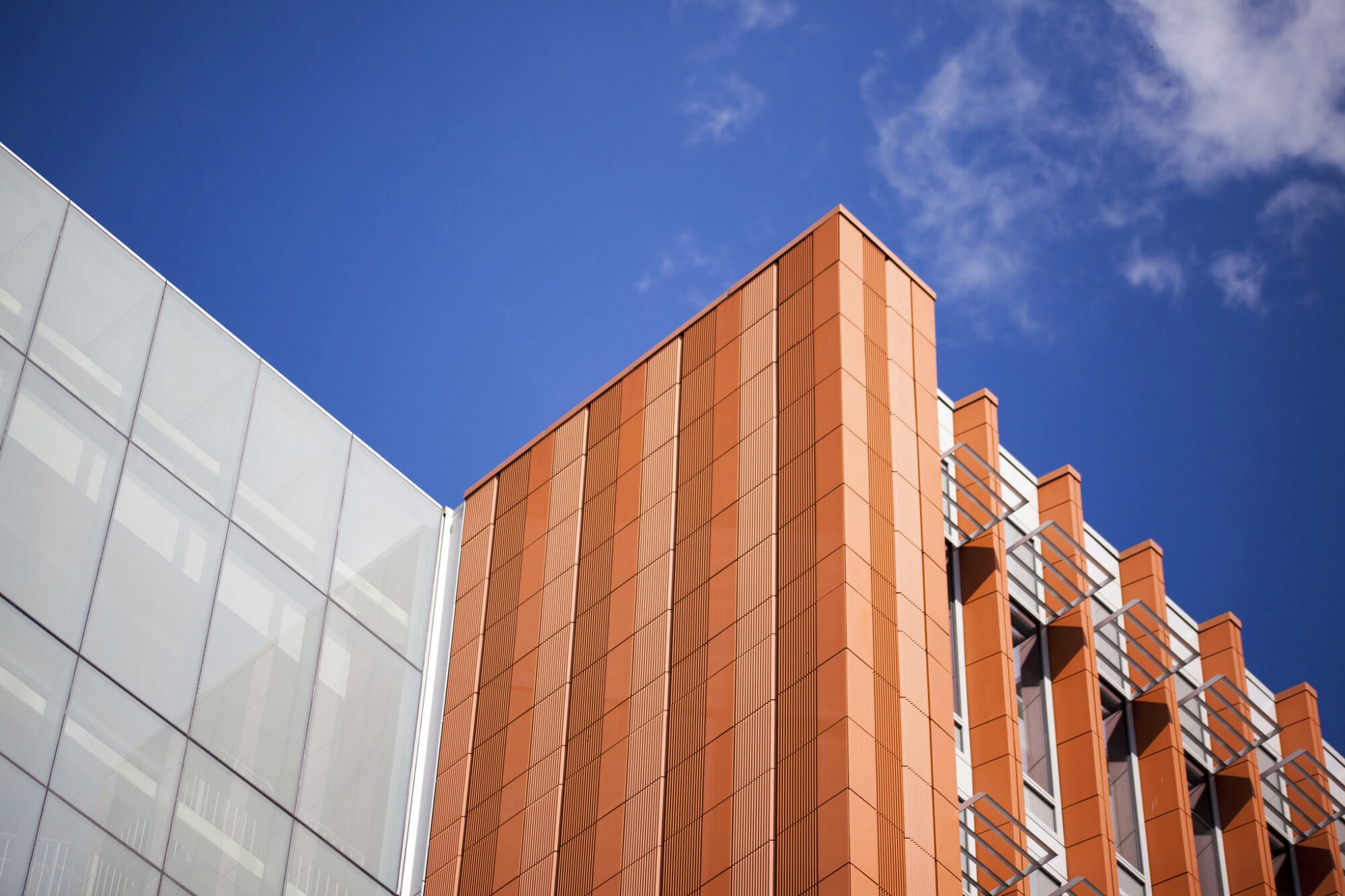 Close-up of a modern building featuring a textured orange façade against a bright blue sky with scattered clouds.