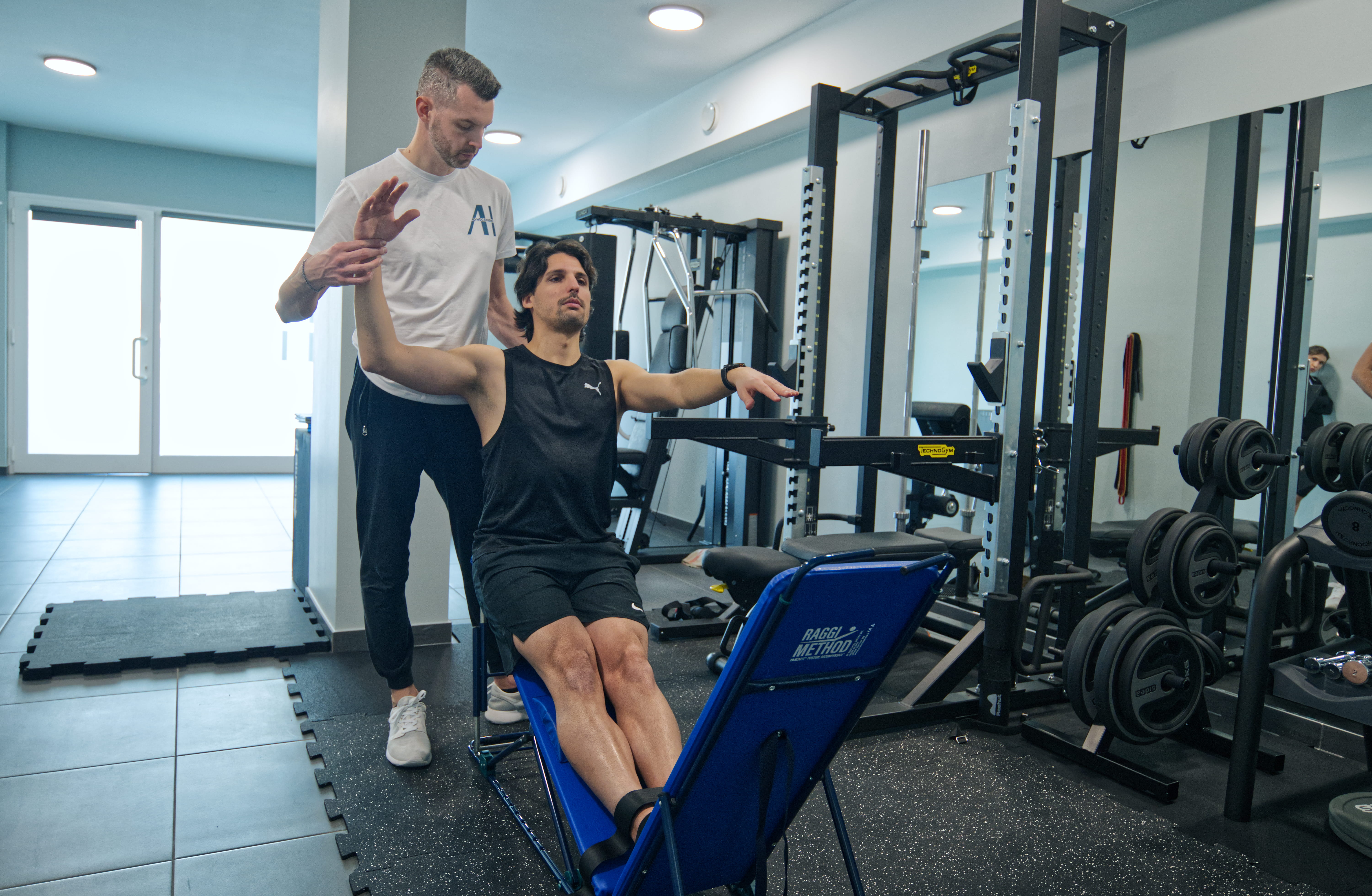 A man and woman sit on beige chairs in a modern room with a red paneled wall. A red pendant light hangs above a wooden coffee table between them.