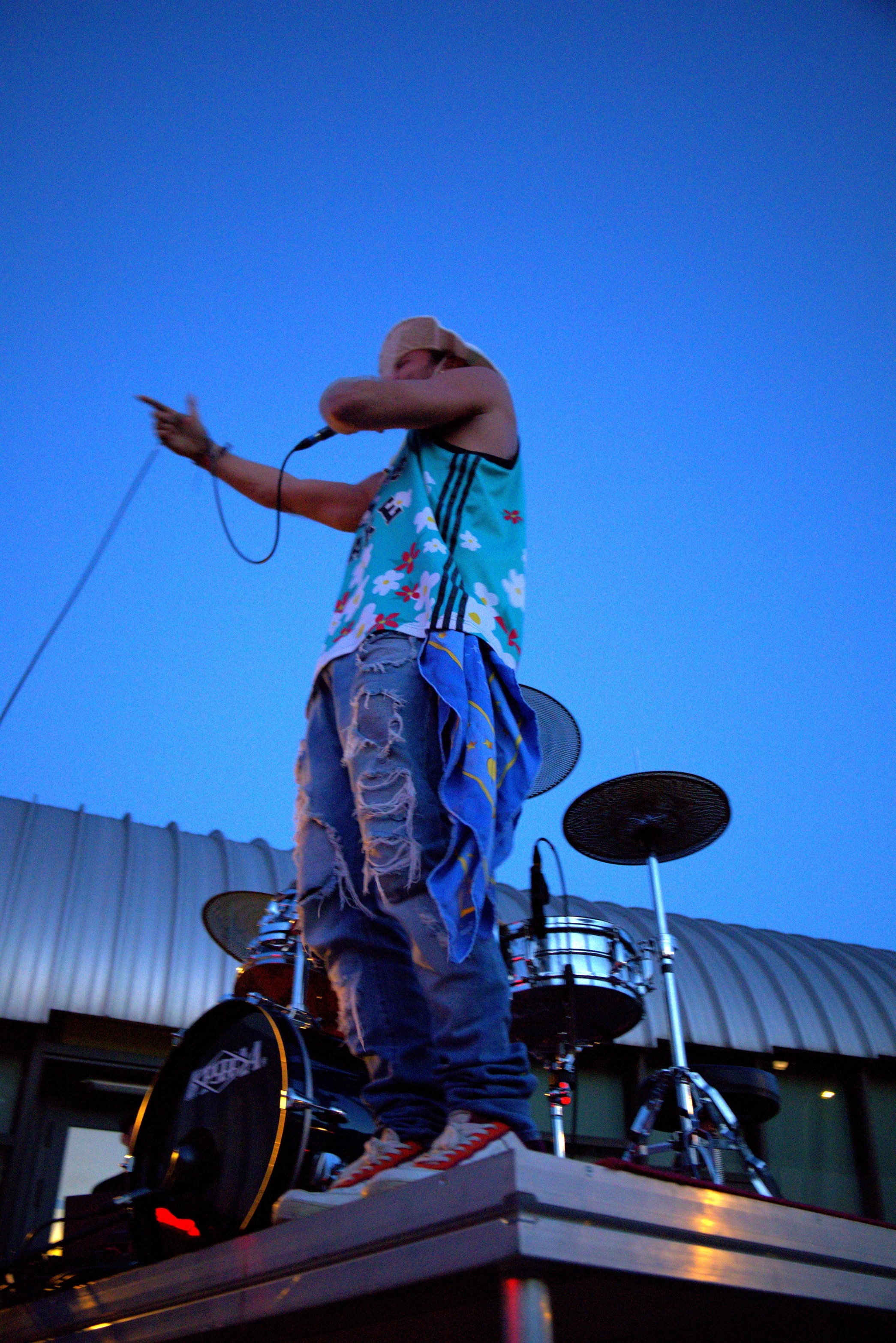 A performer in a colorful outfit stands on a platform, gesturing against a twilight sky.
