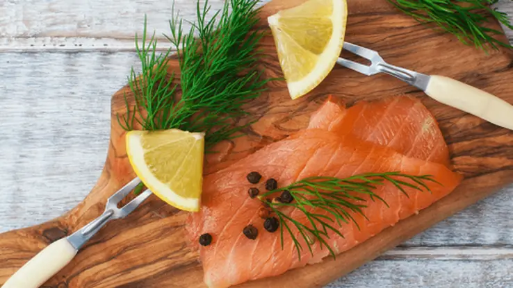 Fresh salmon fillets garnished with dill and lemon on a wooden serving board.