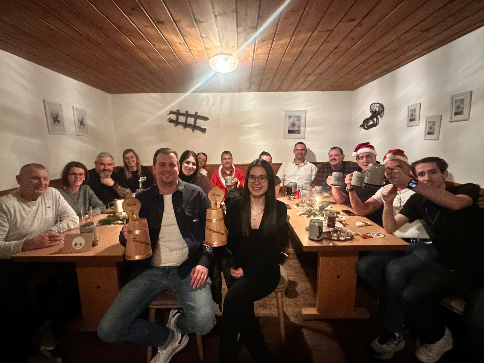 A smiling man with curly hair is sitting at a desk, looking at the camera, with a laptop and a lamp in the background.
