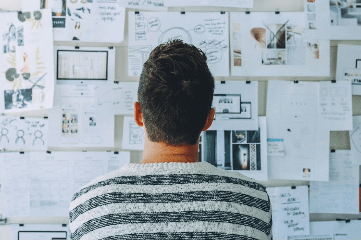 A Man Wearing Black and White Striped Shirt Looking at White Printer Papers on the Wall