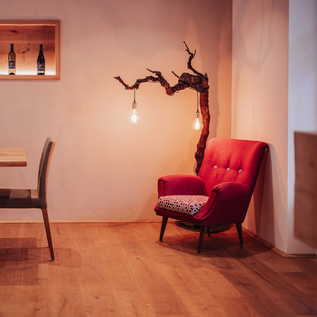 Professionelle Gastronomie- & Interieur-Fotografie: Gemütliche Lounge-Ecke mit rotem Sessel und beleuchteter Wein-Präsentation, inszeniert mit warmem Ambient-Licht und Fokus auf Design-Details.