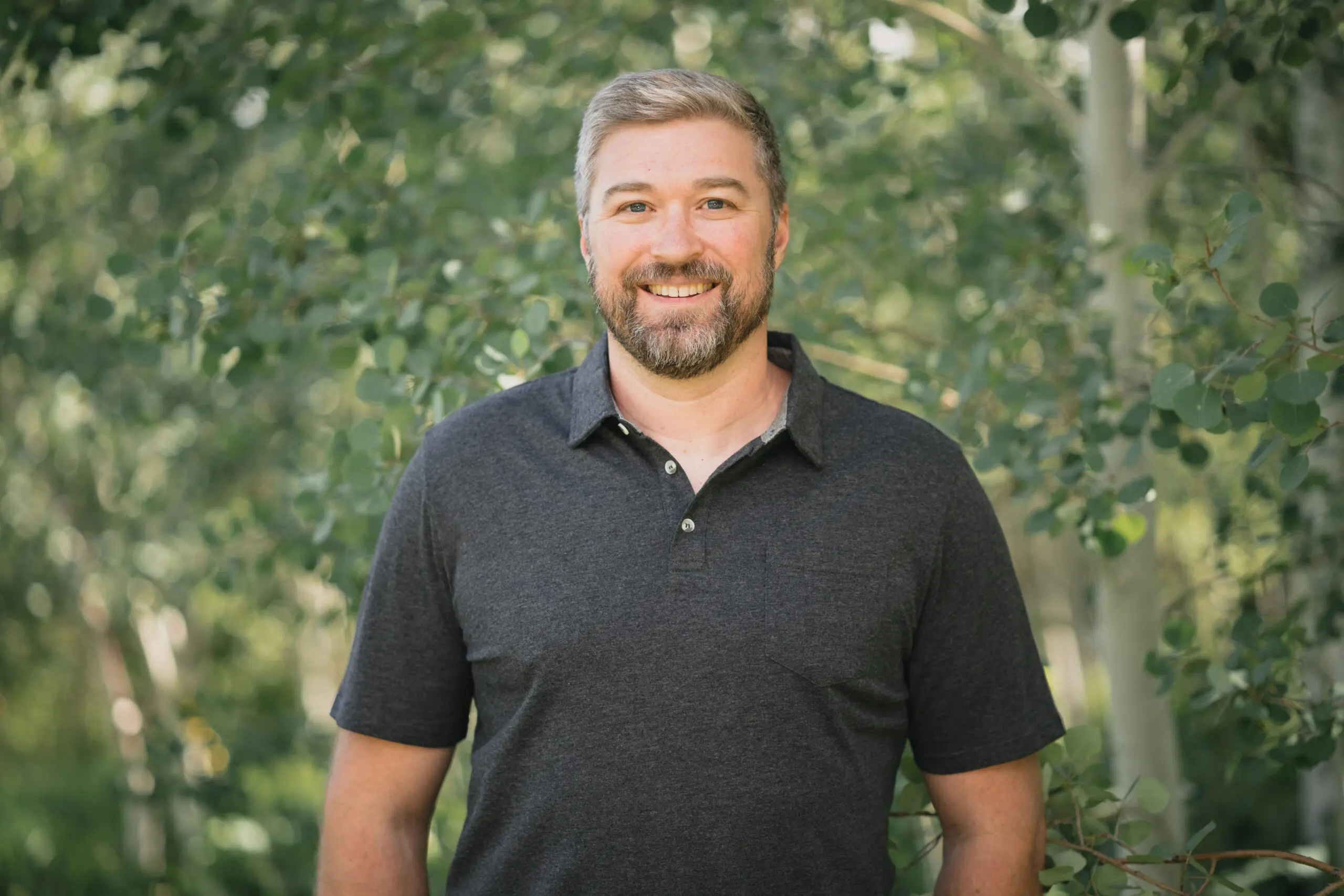 Professional outdoor headshot with softly blurred green foliage.