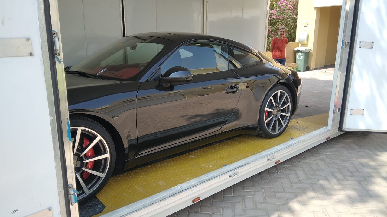 A dark Porsche 911 with red interior is in an enclosed car shipping haulier to keep it stable for transport.