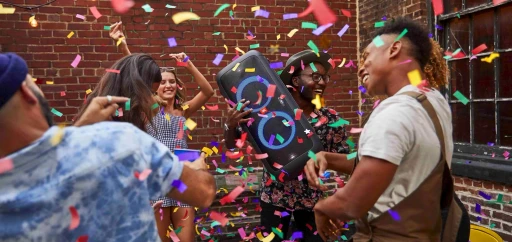 A group of friends partying outdoors with a large speaker and confetti everywhere