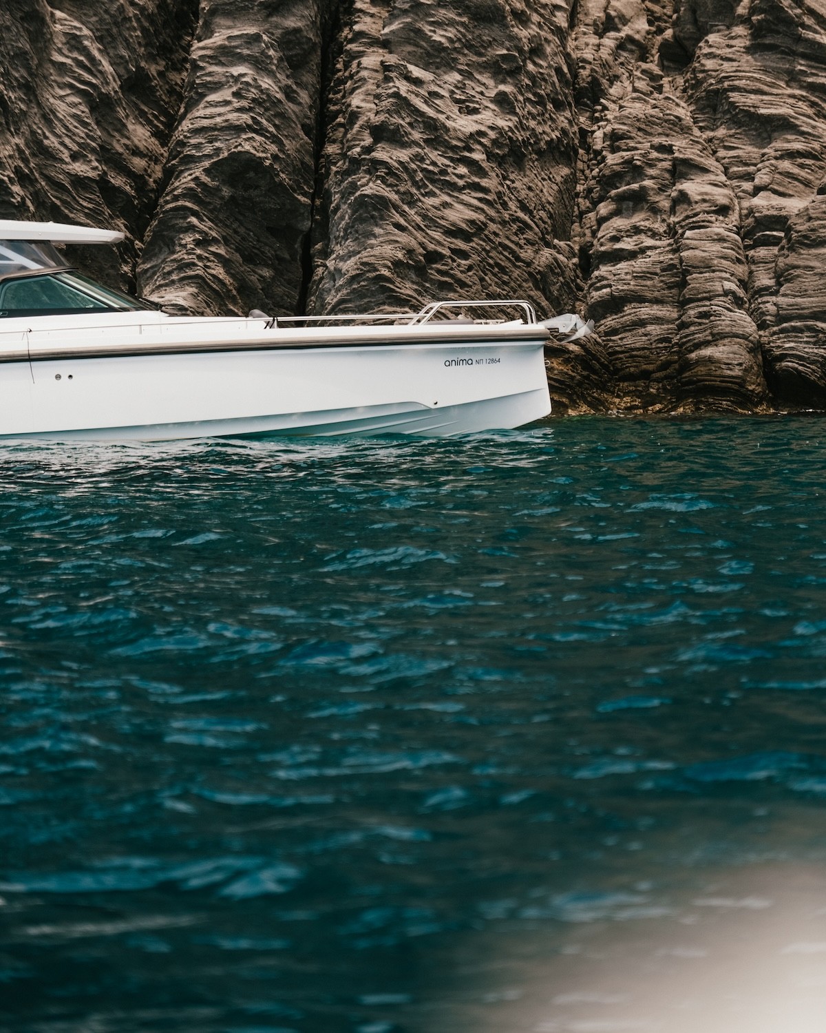 White Axopar 37 motor yacht anchored in crystal-clear turquoise waters near dramatic white limestone cliffs in the Cyclades.