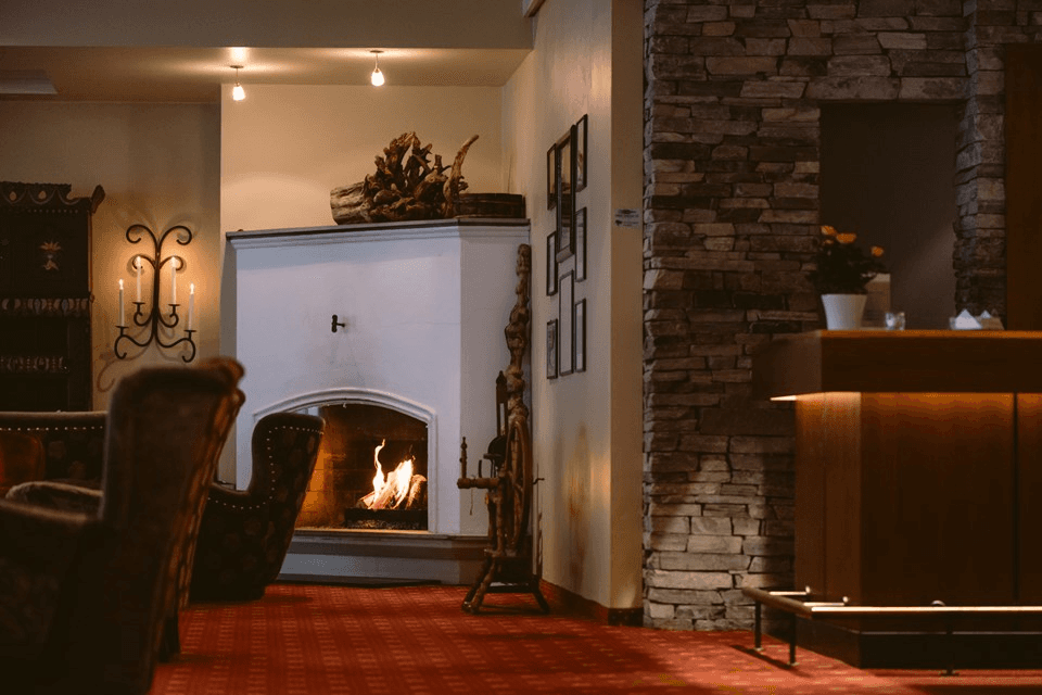 Cozy interior of a room with a fireplace, wooden furniture, and a bar area, featuring warm lighting and a red carpet.