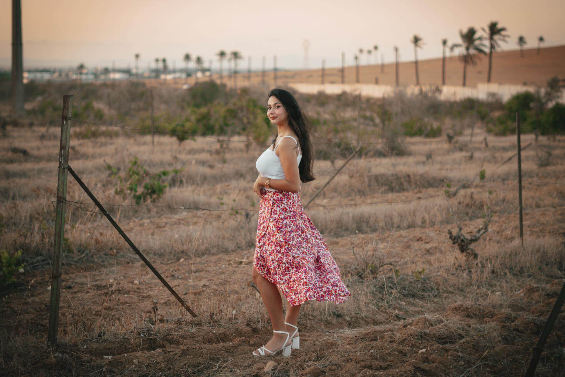 A woman in a pink skirt stands gracefully in a vibrant green field, surrounded by nature's beauty