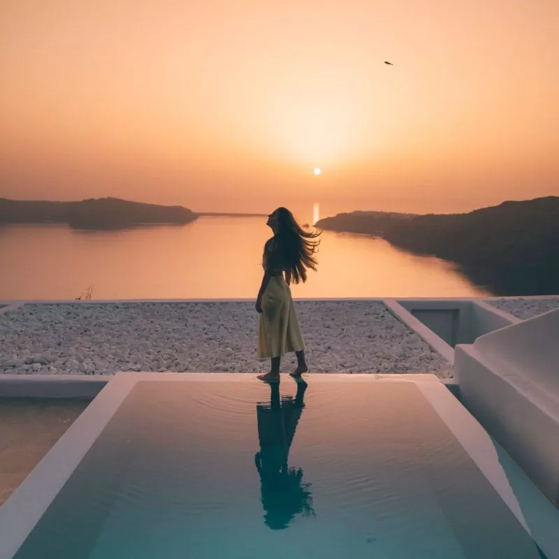 Frau genießt Sonnenuntergang am Pool in Santorini