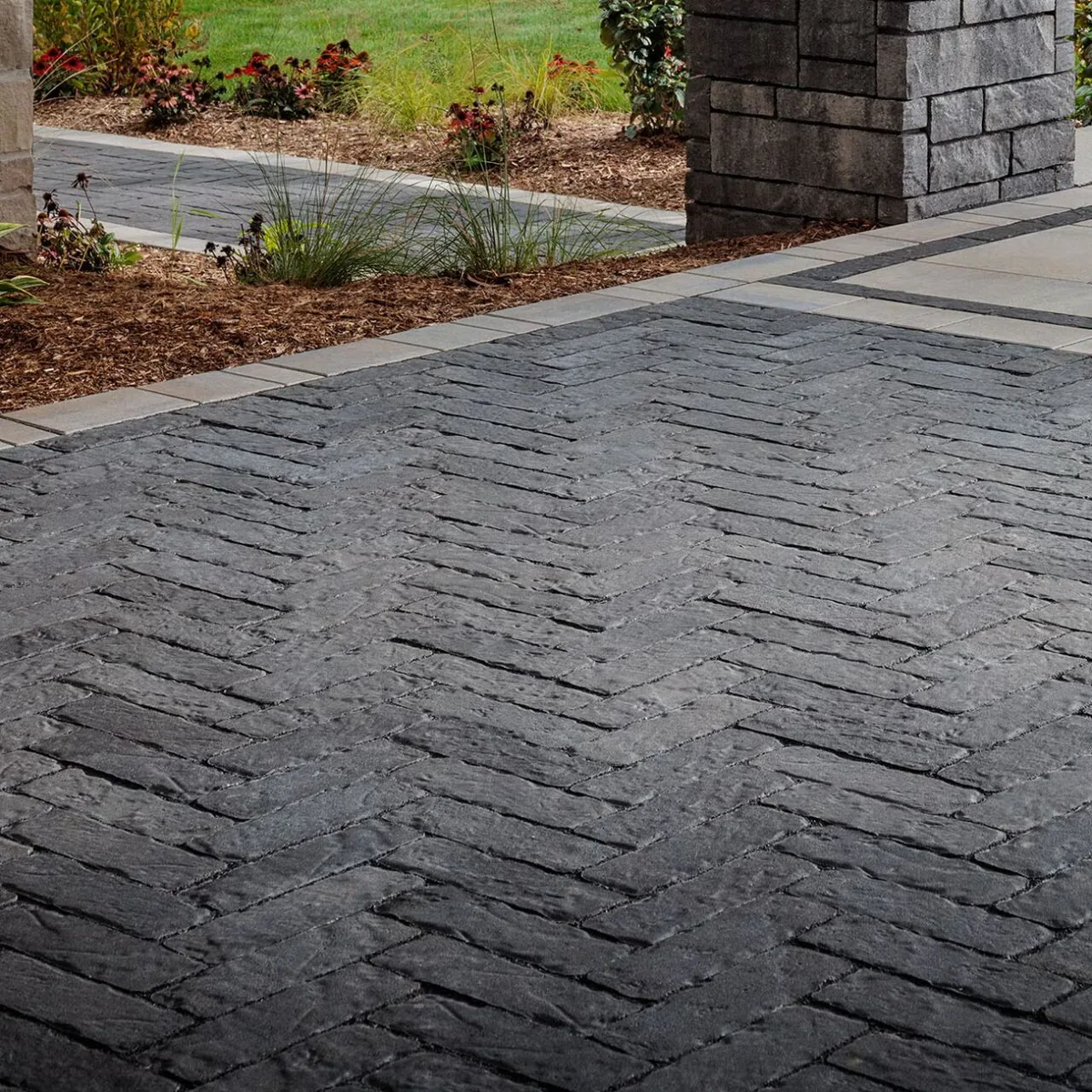 Dark textured pavers laid in an interlocking pattern beside a planted border.