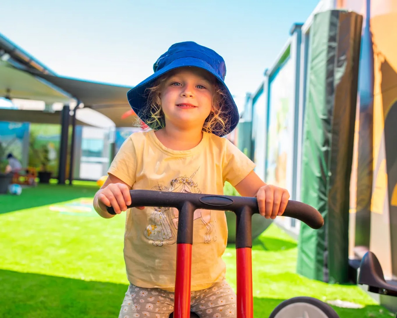 Child smiling while riding a scooter in the outdoor play area at Kaleidoscope Kids childcare in Brisbane.