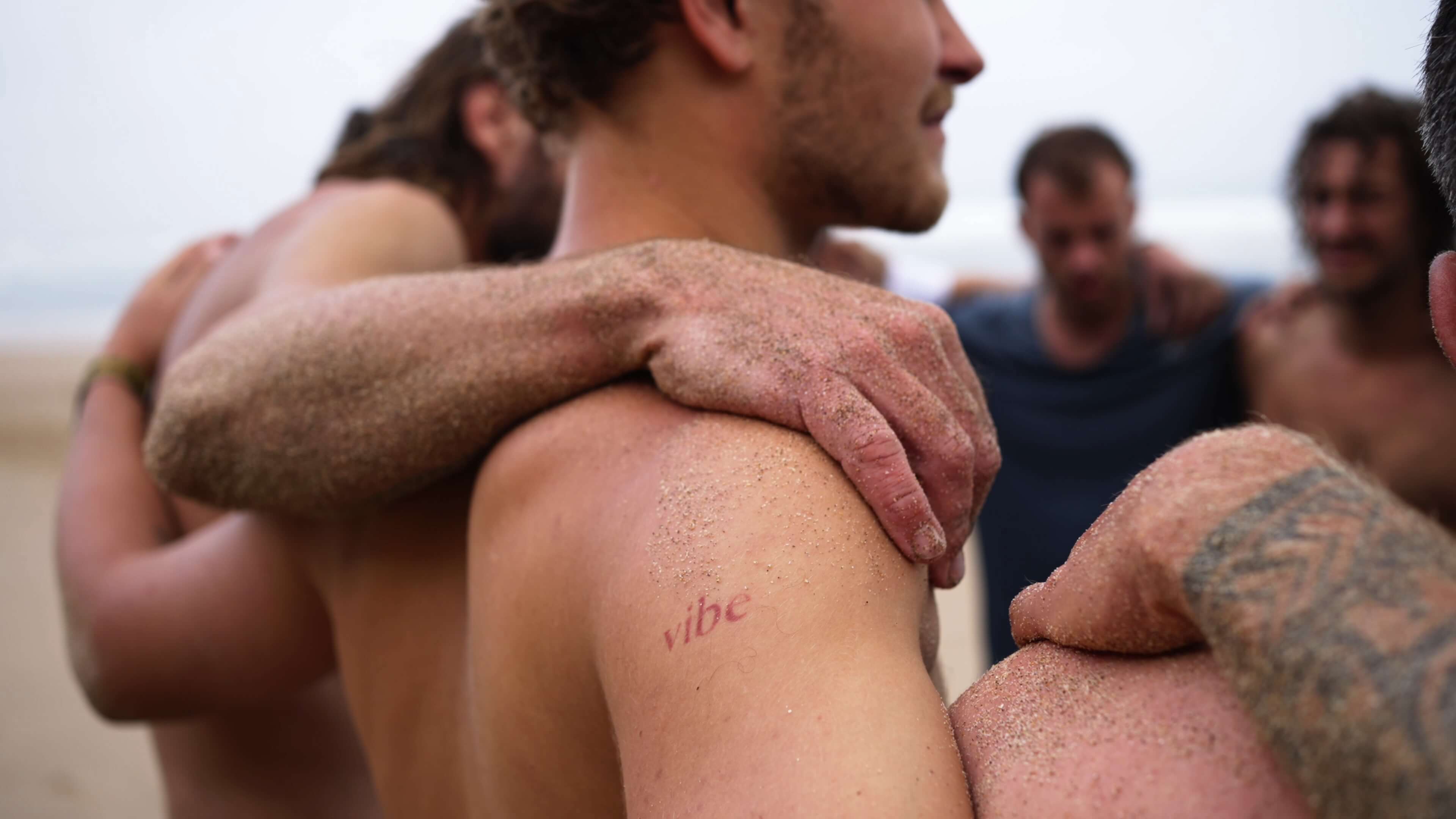 Close up of a circle of men on the beach with arms interlocked