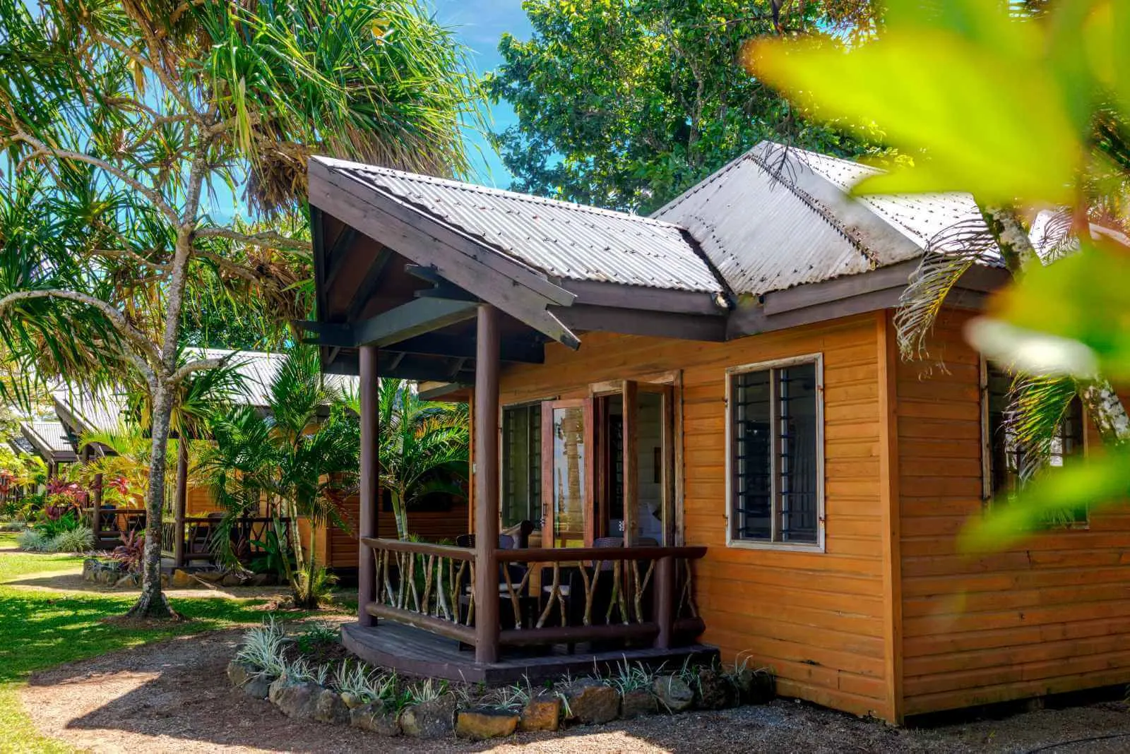 Traditional Fiji bure in garden setting with dark roofs nestled amidst lush tropical greenery at Uprising Beach Resort.