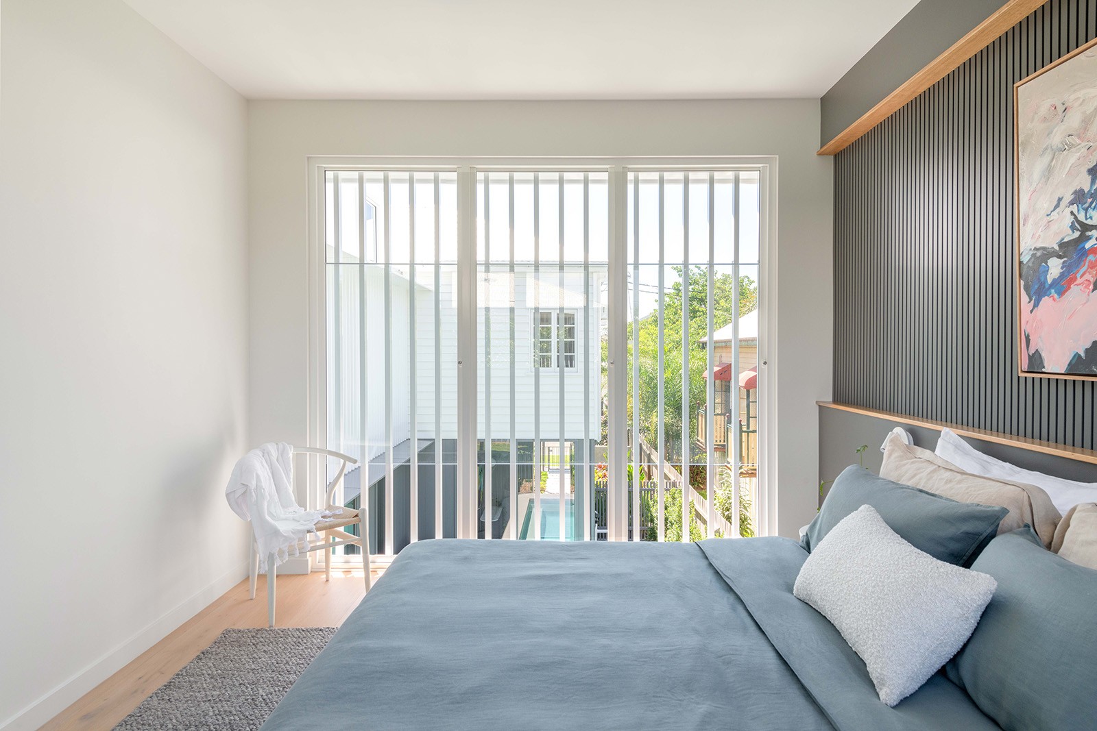 Bedroom interior at The Stables featuring soft furnishings, timber accents, and filtered daylight through battened glazing.