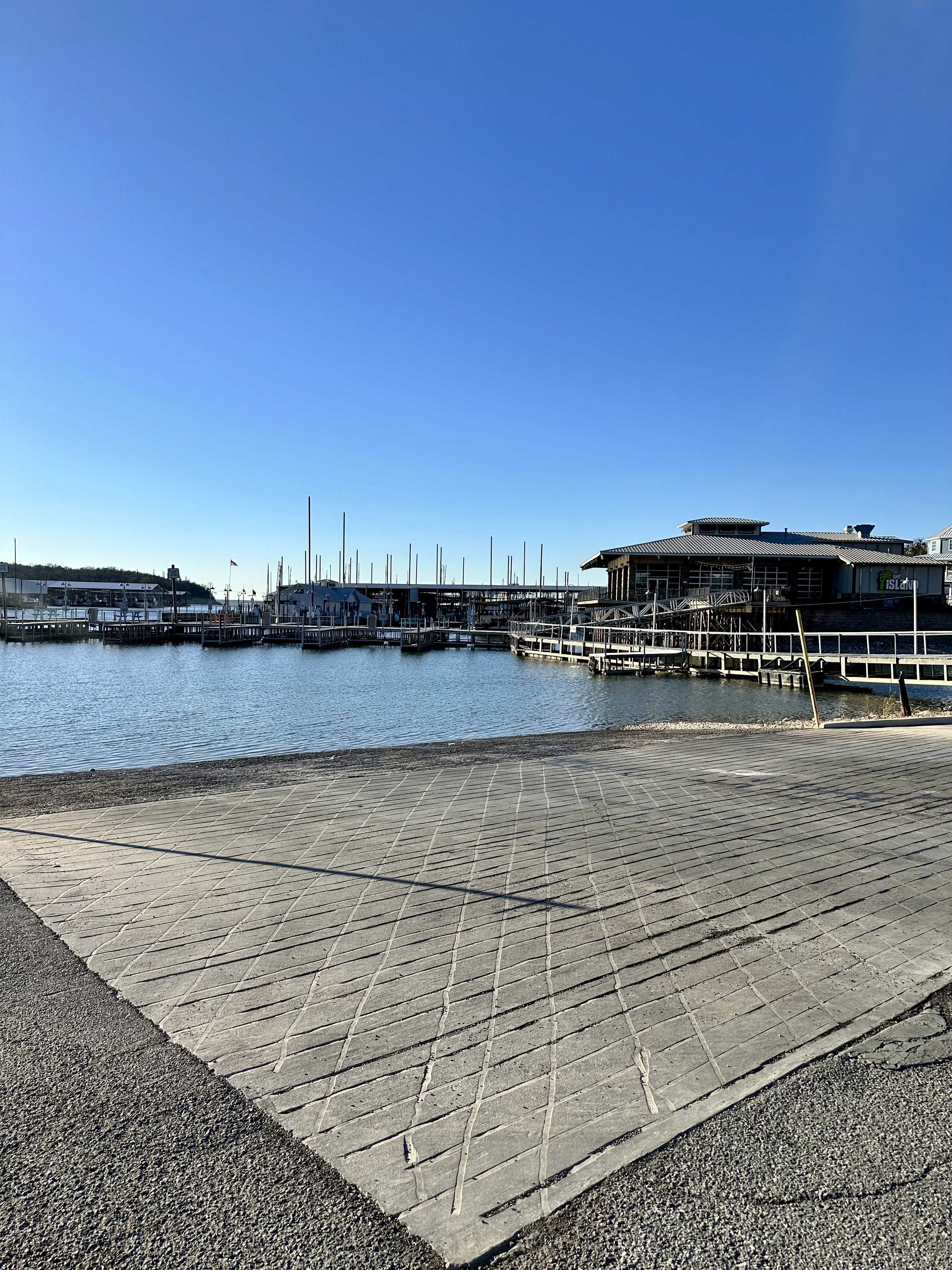 A sleek, modern pontoon boat with a blue and silver metallic finish is docked in a covered marina, reflecting sunlight on the water surface.