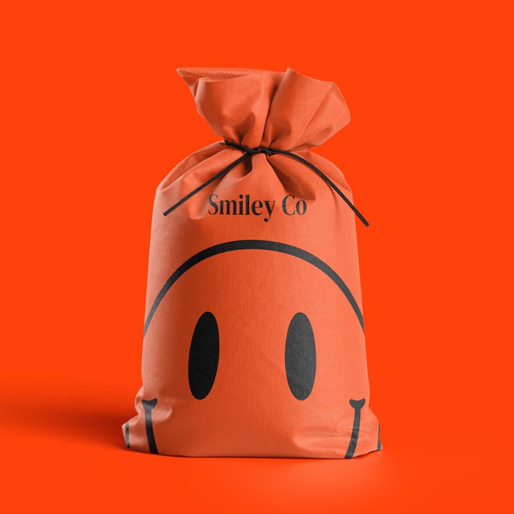 Bright orange drawstring fabric bag tied at the top, printed with a bold black smiley face and the text “Smiley Co” above it against an orange background.