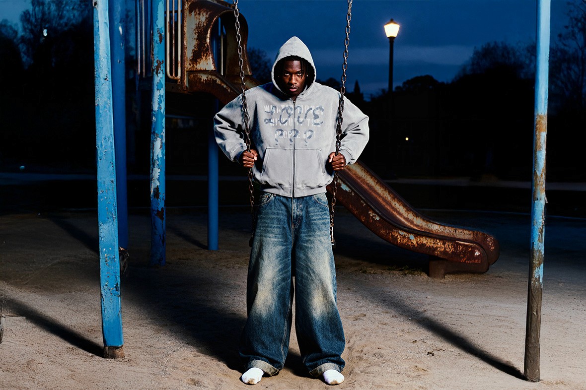 Male model in gray oversized hoodie posing in an empty playground, part of Youth Distortion streetwear campaign.