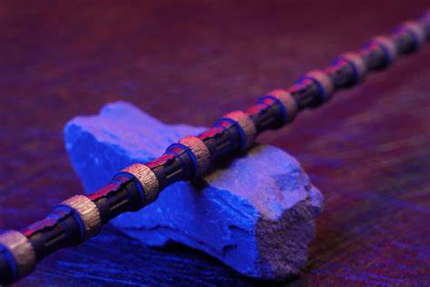 A close-up of a diamond wire saw placed on a blue stone under special lighting. The wire’s cutting segments are clearly visible, designed for slicing through hard materials like stone and concrete.