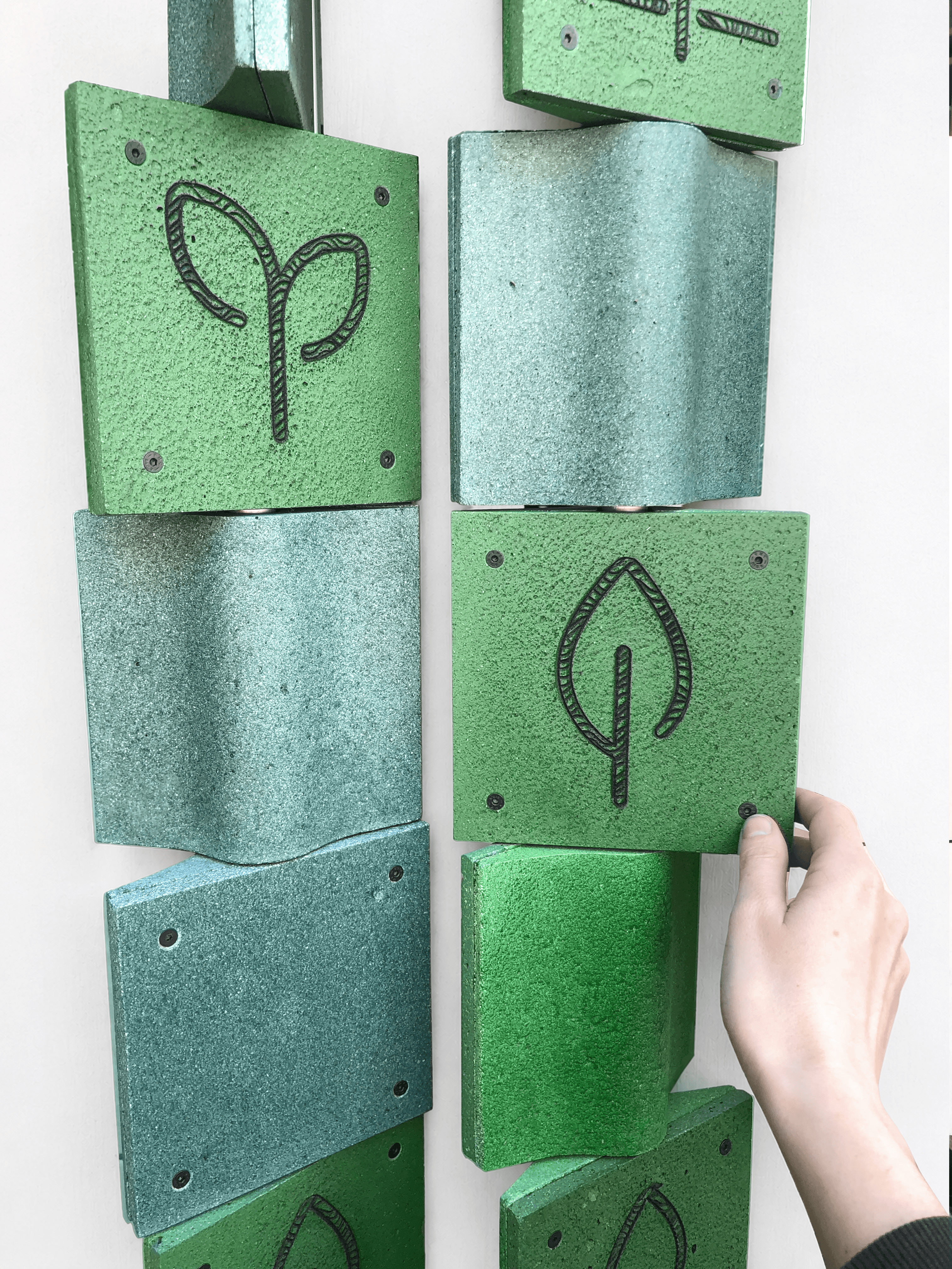 Close-up of rotating green composite tiles engraved with plant-inspired symbols as part of the DIAPHRAGM interactive wall installation.