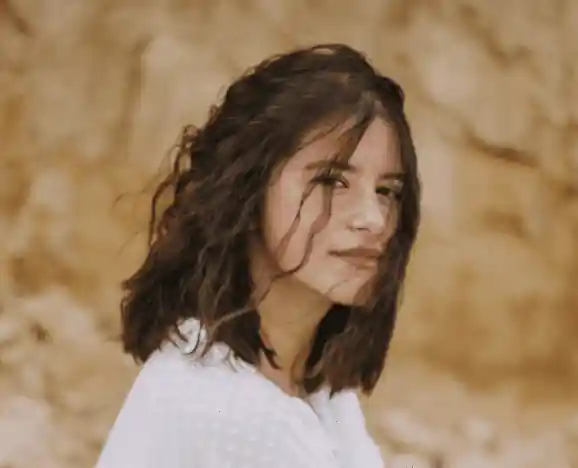 Jeune femme brune avec un chignon dehors devant un bâtiment orange et blanc