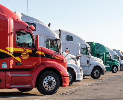 Line of colorful semi-trucks parked side by side in a lot under daylight.