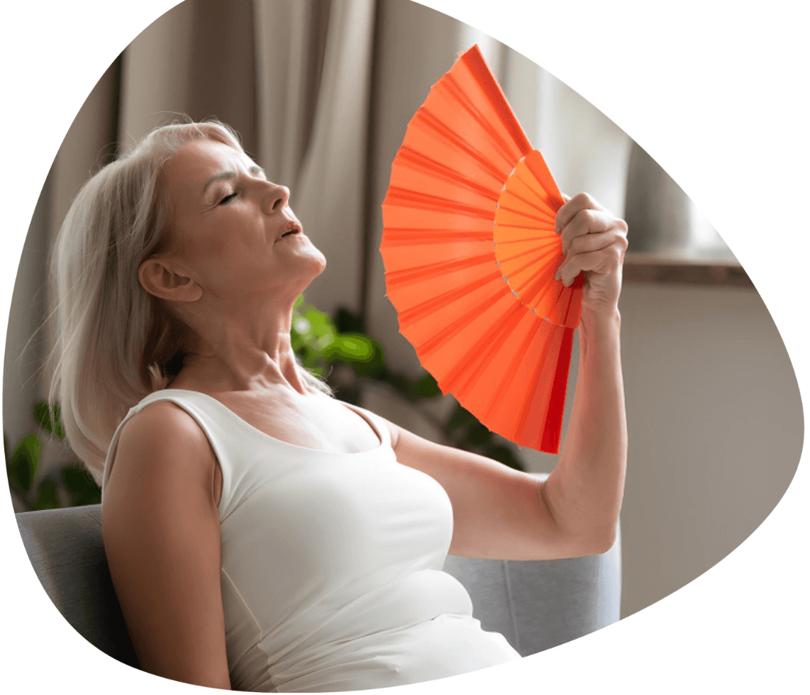 Woman cooling herself with a hand fan, representing menopause health insurance cover and benefits
