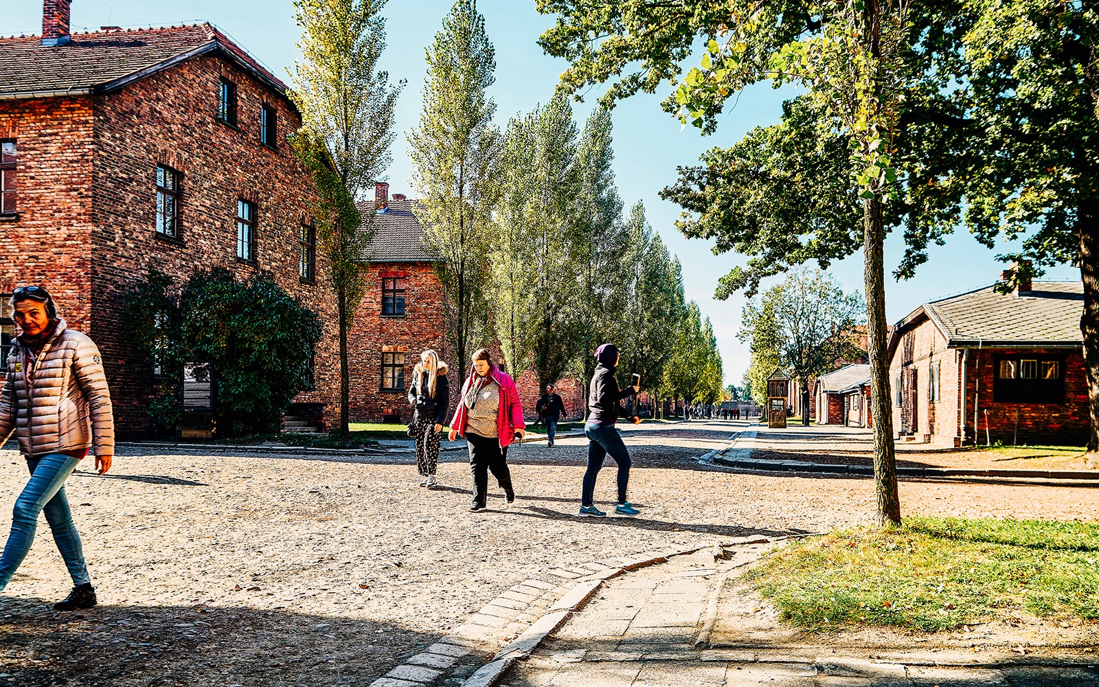 Besökare som promenerar genom Auschwitz-Birkenau med tegelbyggnader och träd i sikte.