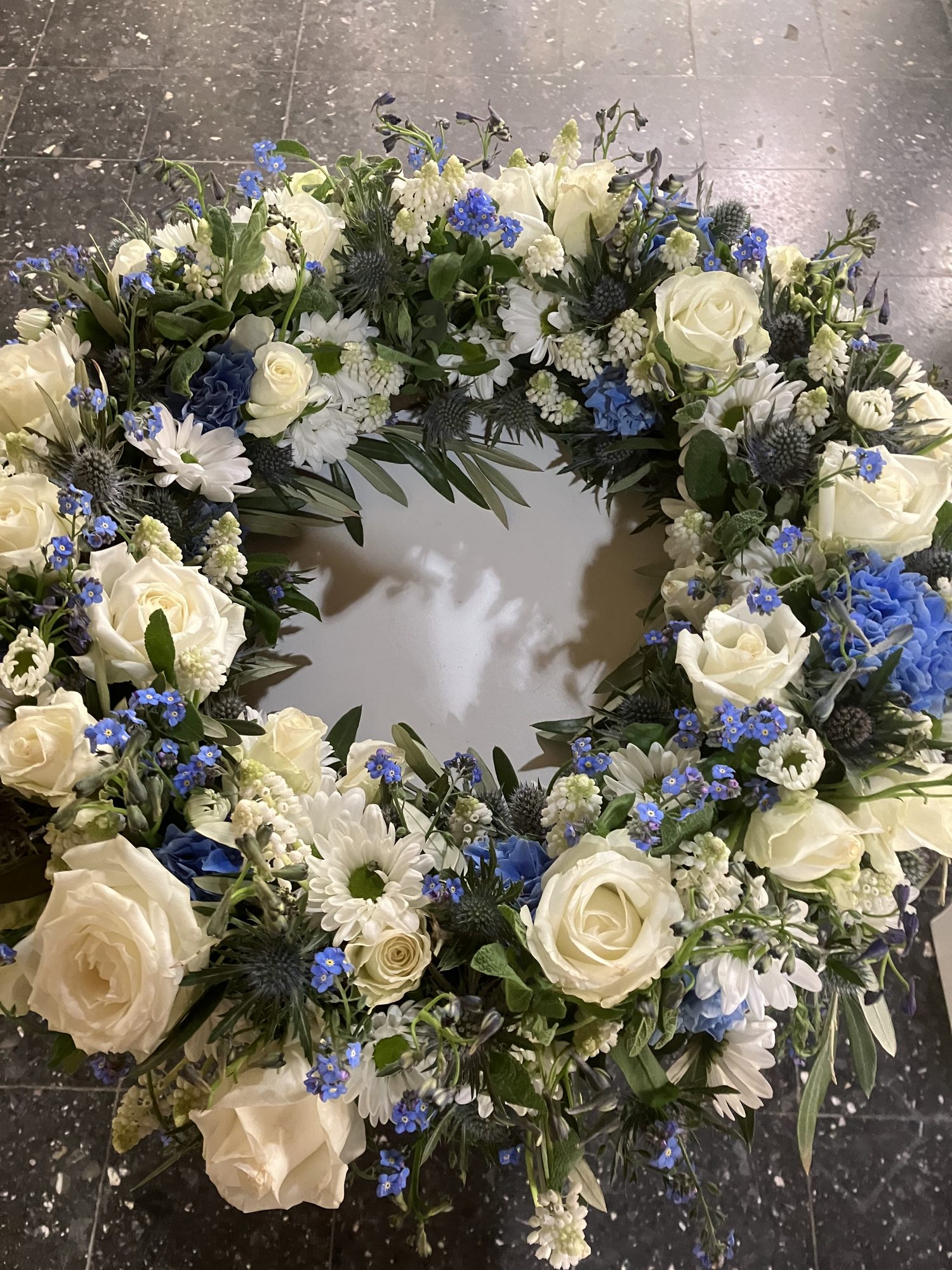 Trauerkranz aus weißen Rosen und blauen Blüten