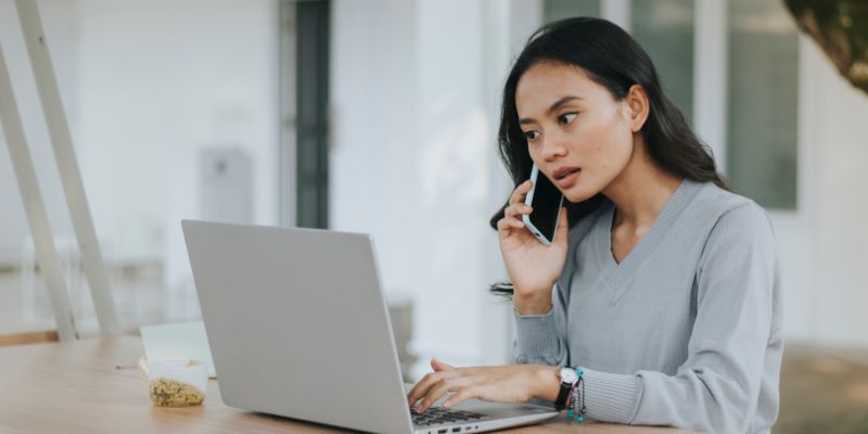 A Malaysian woman talking to someone on the phone while typing on her laptop