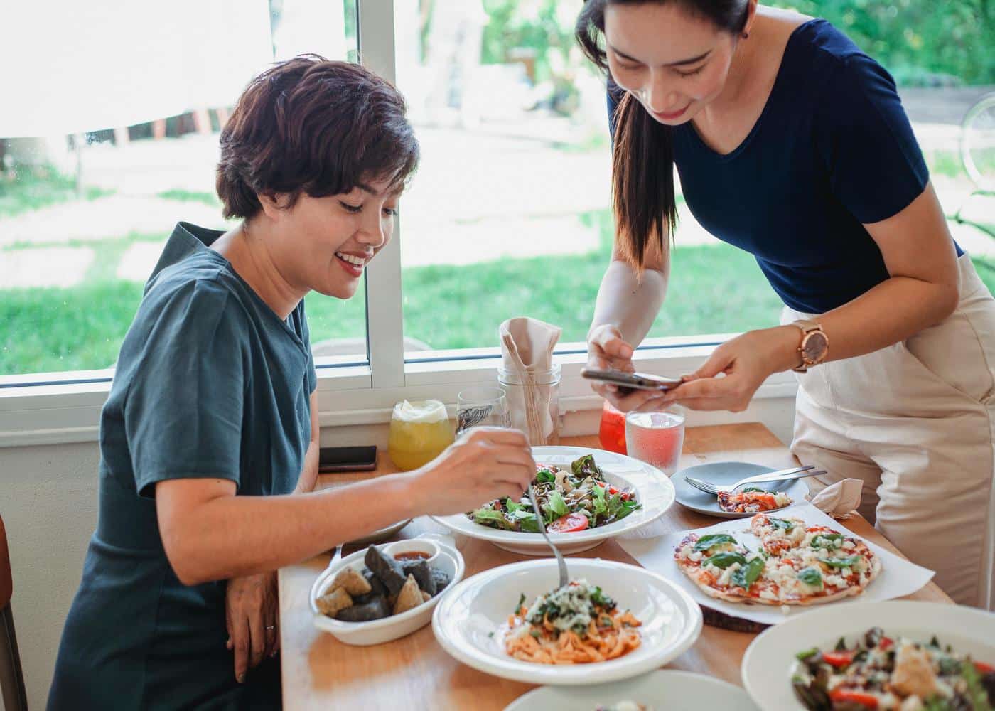Two women with food in fron of them while one of them is holding smartphone over food