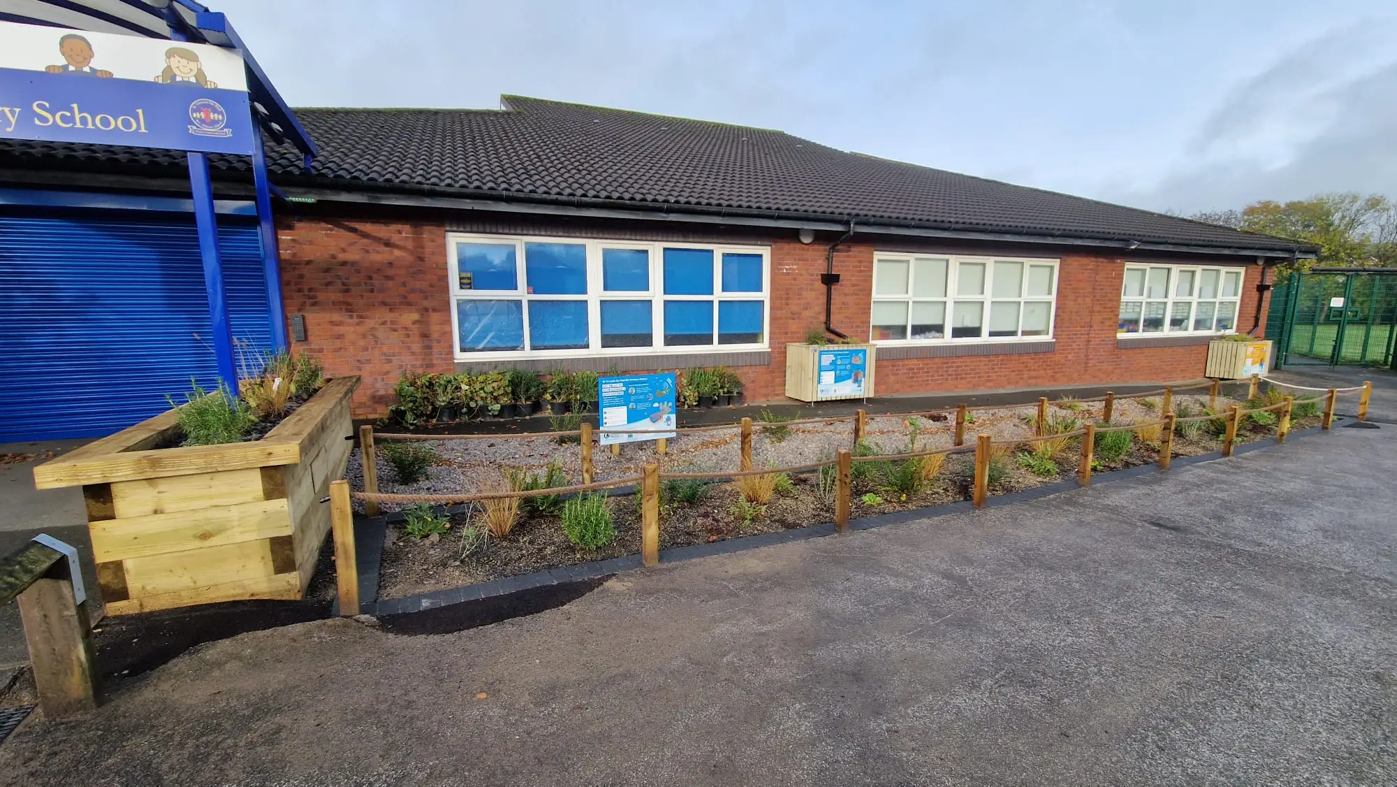 A brick building with blue windows, surrounded by plants and gravel, and a yellow machine in the foreground.