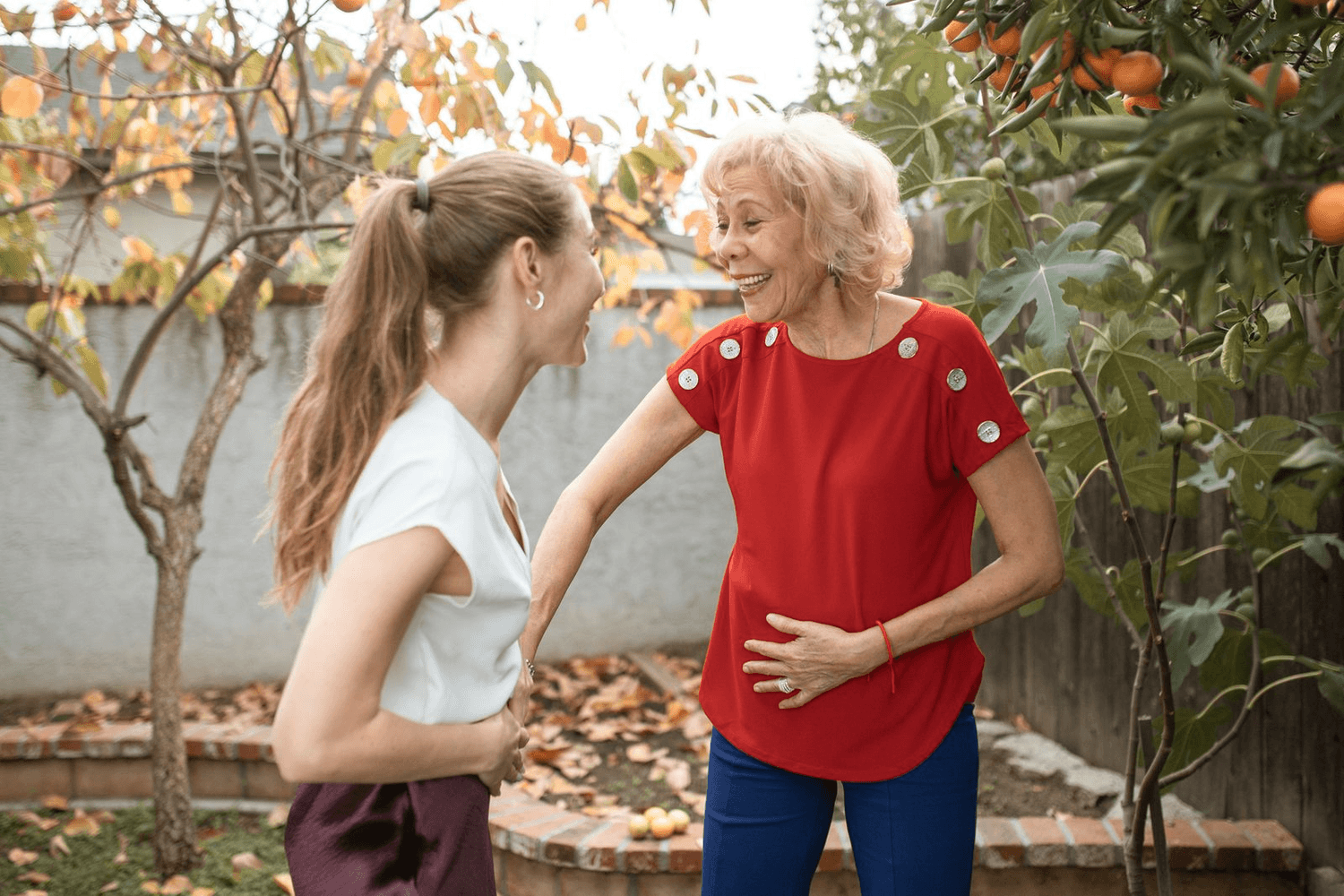 An older woman laughs with her daughter in a sunny garden.