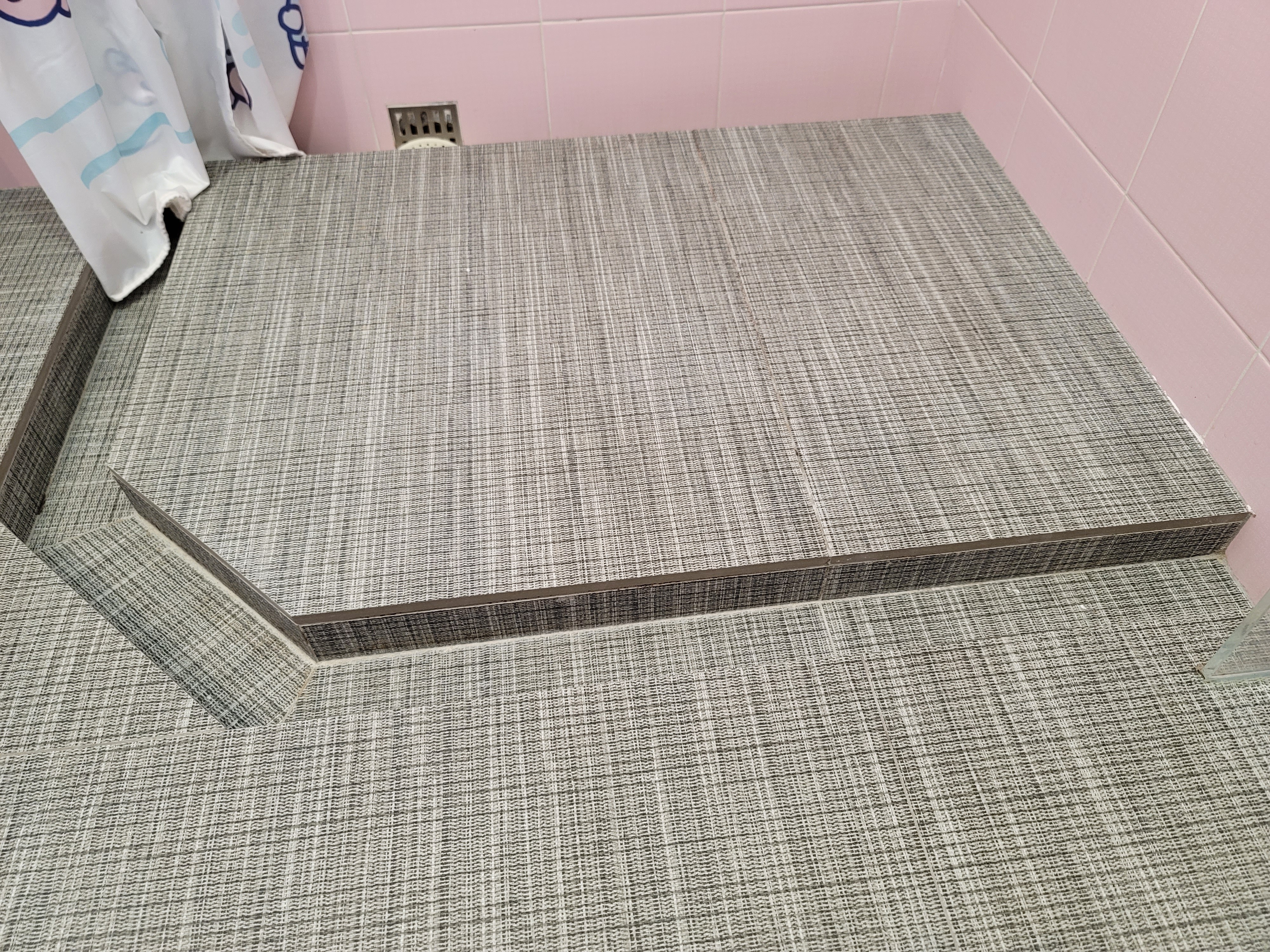 Close-up of gray textured vinyl floor tiles and pink ceramic wall tiles in a small bathroom design 3x2 at Hoi Tat Estate.