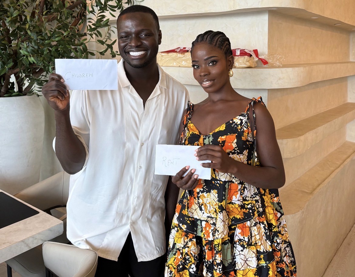 A person sits at a cluttered desk in a dimly lit room, focused on two monitors displaying aerial maps. The walls are covered with various images and notes.