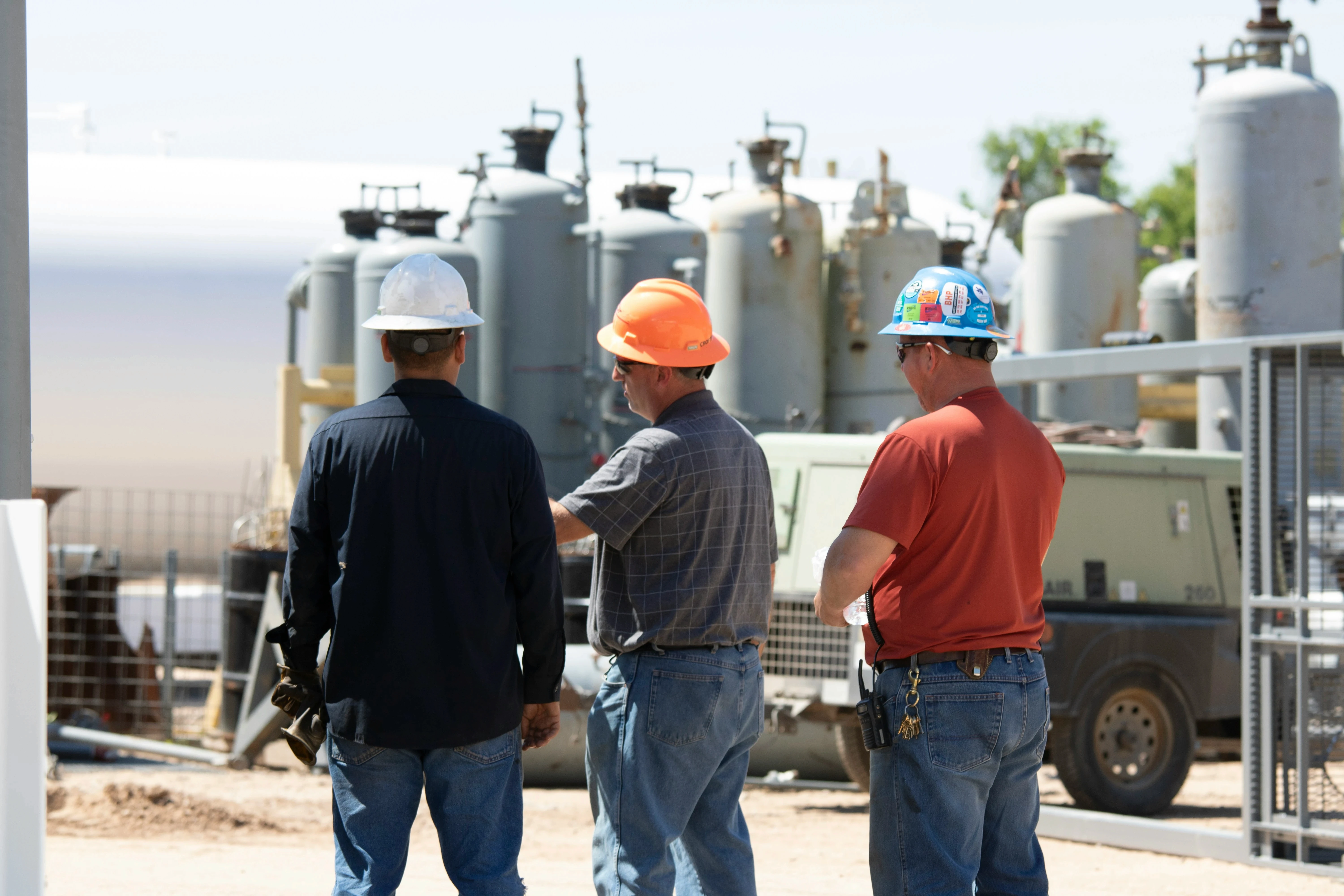 Three engineers in hard hats discussing operations at a natural gas processing facility.