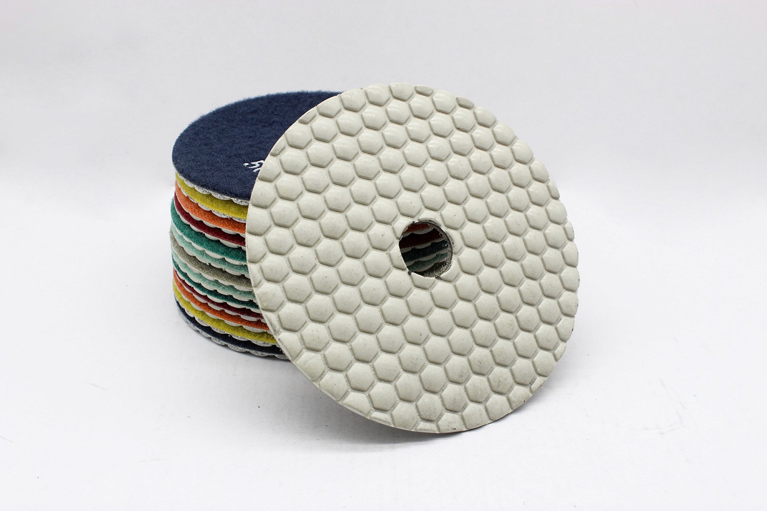 A stack of colorful resin bond diamond polishing pads, with one pad displaying a hexagonal pattern.